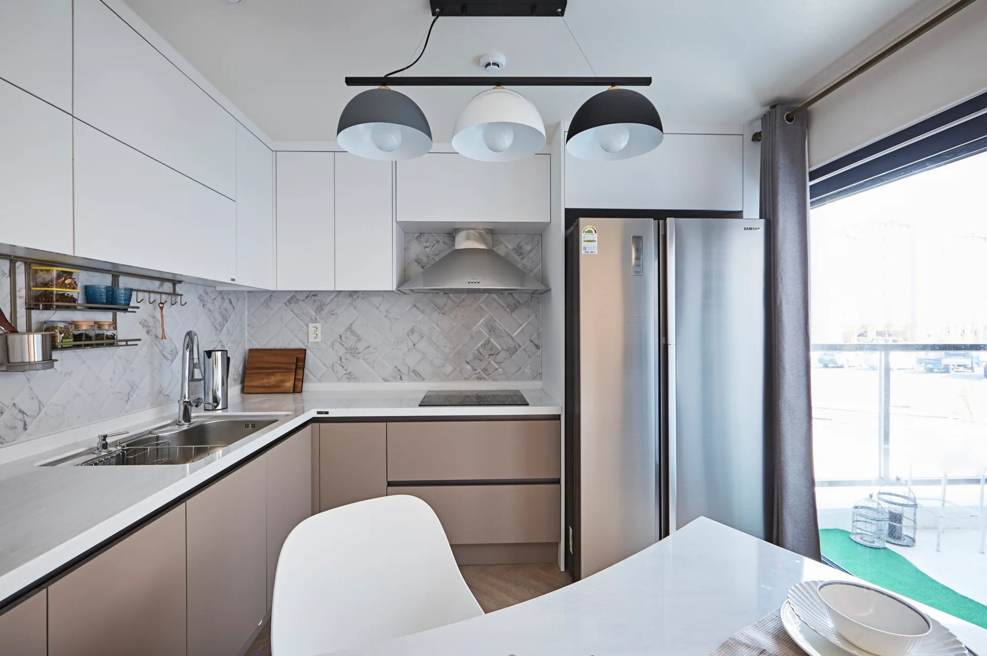 A modern kitchen featuring two-toned white and beige cabinets, a marble herringbone tile backsplash, and stainless steel appliances.