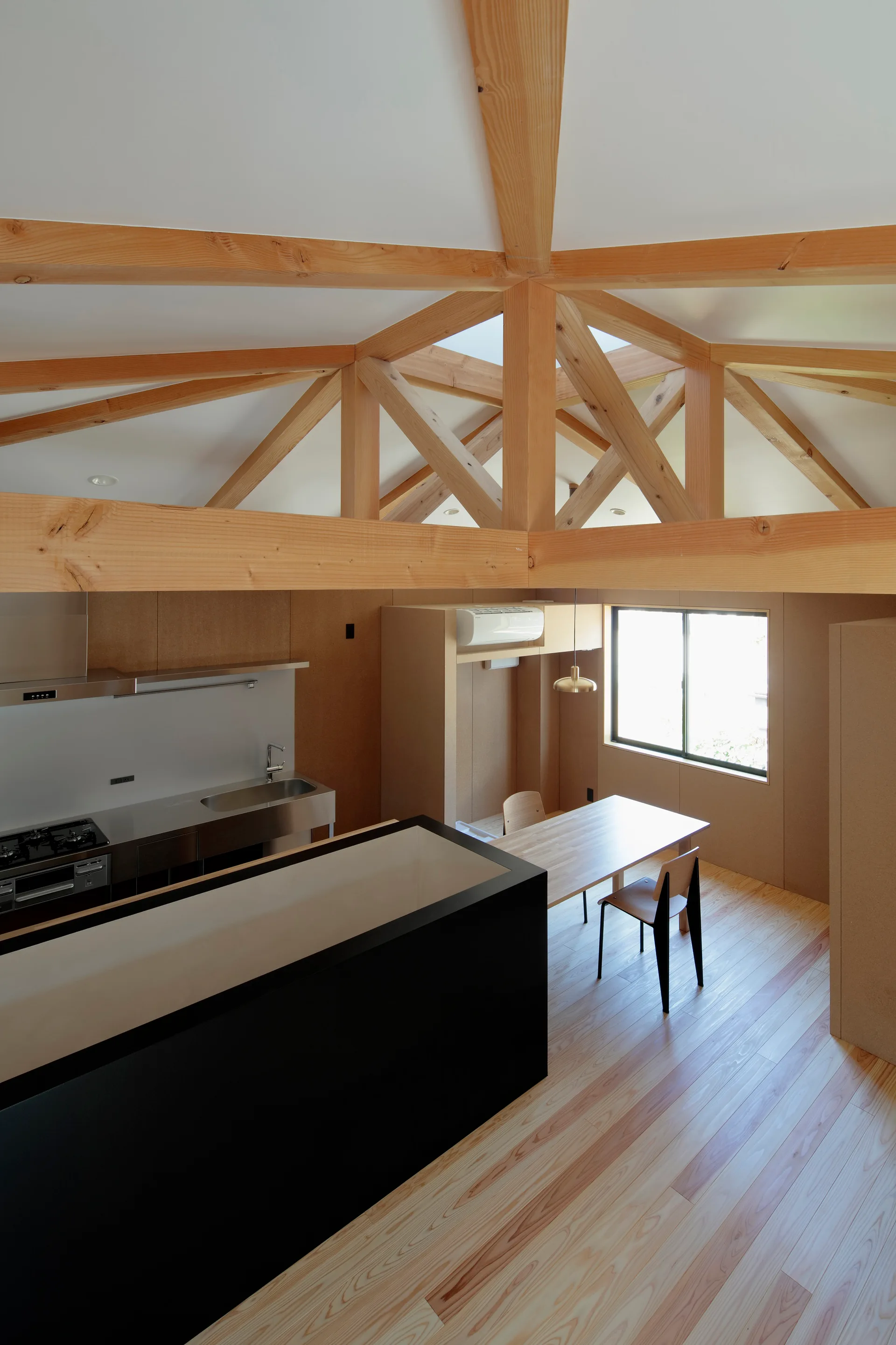 An open-plan kitchen and dining area features an exposed timber truss ceiling, a black kitchen island, and a light wood dining table by a window.
