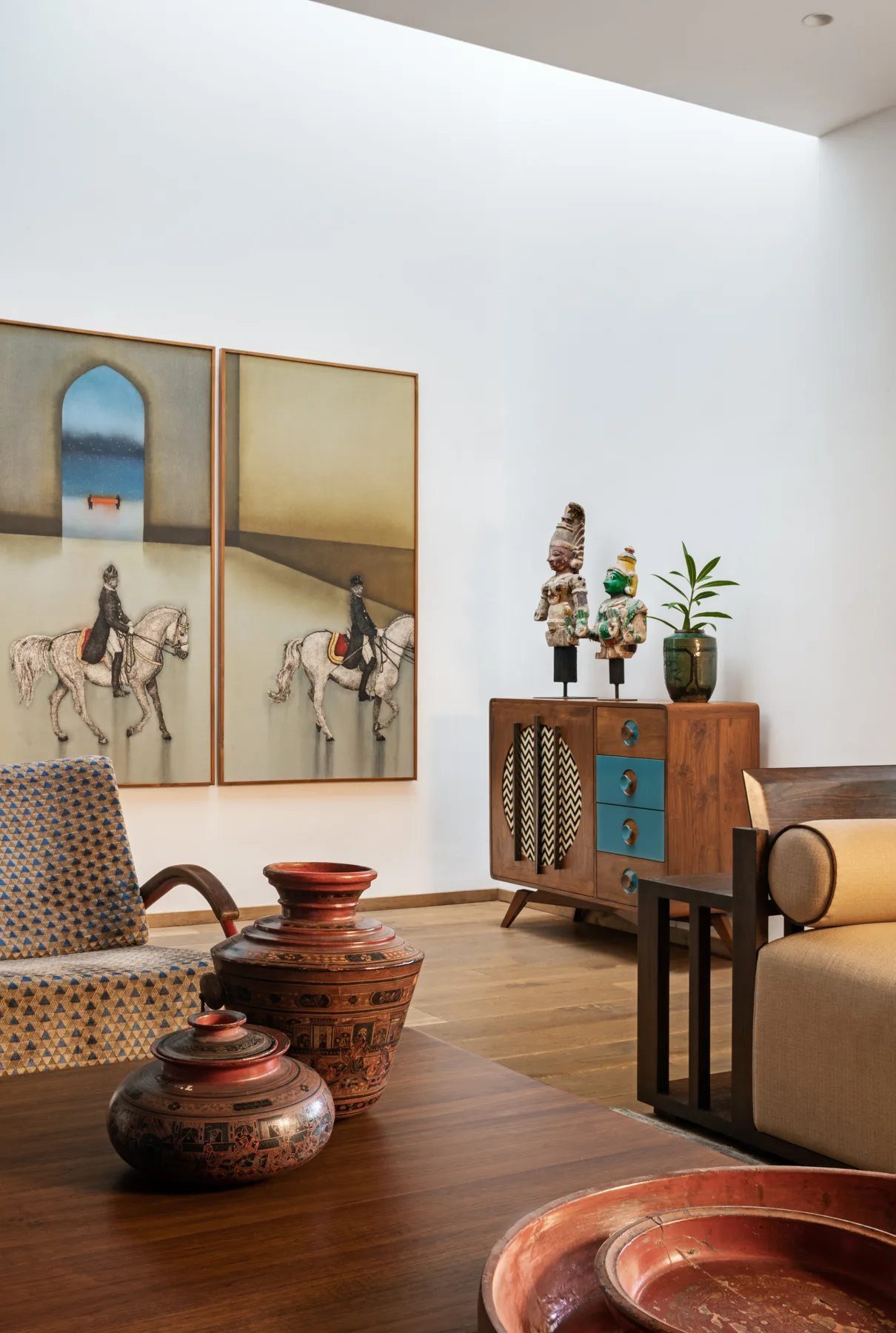A brightly lit living room features a wooden coffee table with ceramic vases, a patterned armchair, and a mid-century sideboard with blue drawers.
