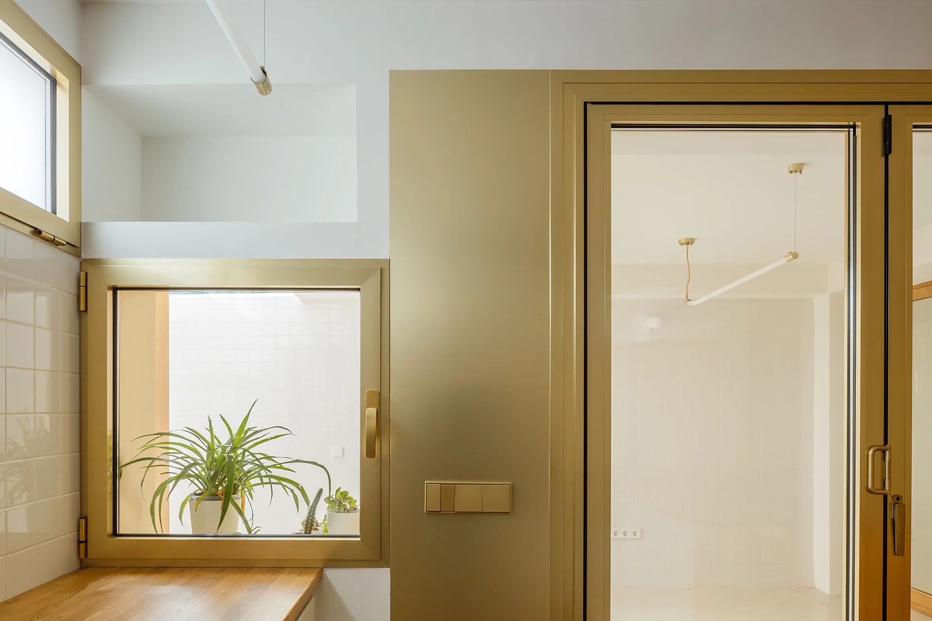 Satin gold metal door and window frames are set into a white plaster wall next to a light wood countertop.