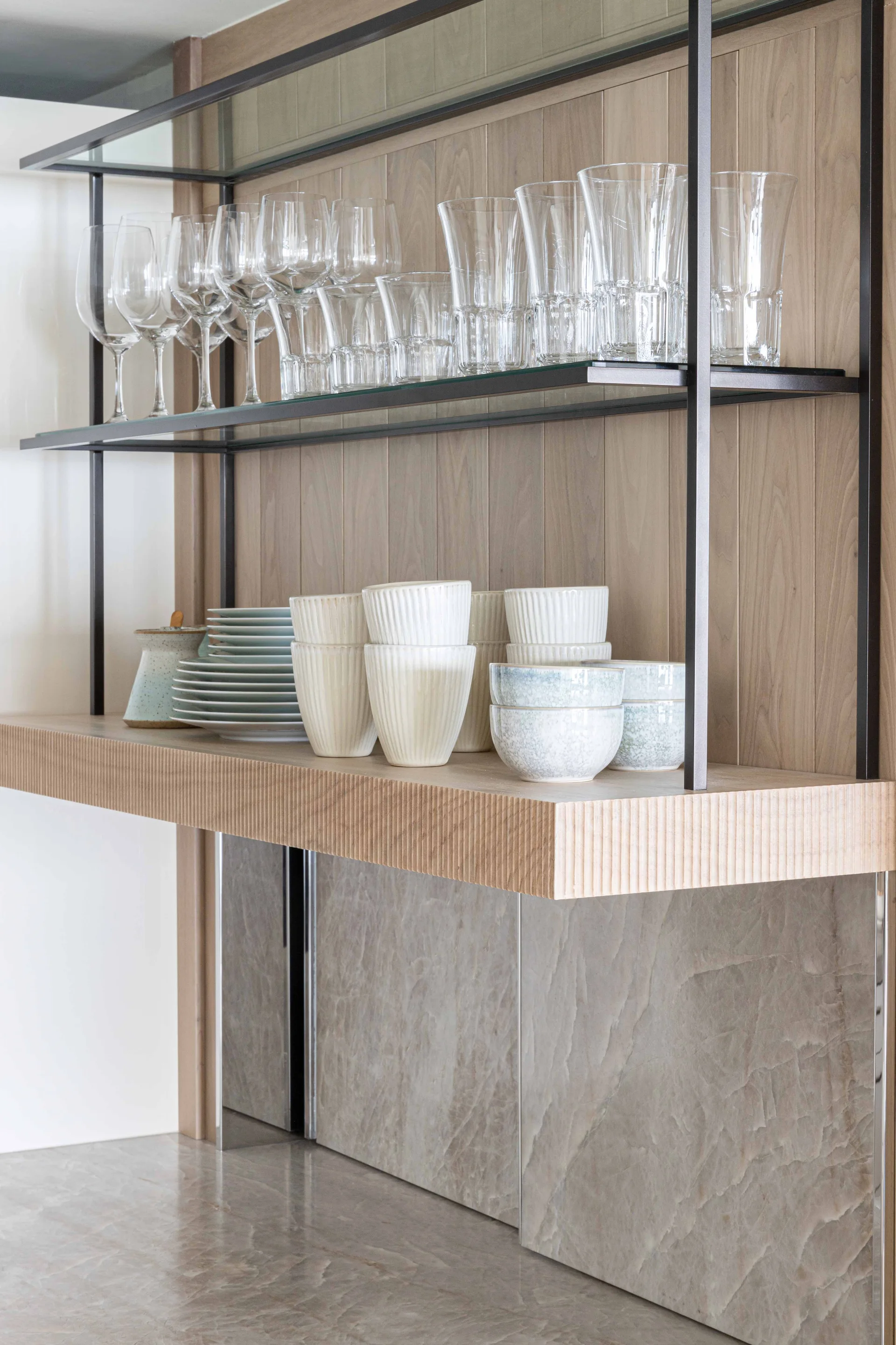 Open kitchen shelving units styled with glassware and ceramic bowls against a vertical wood plank wall.
