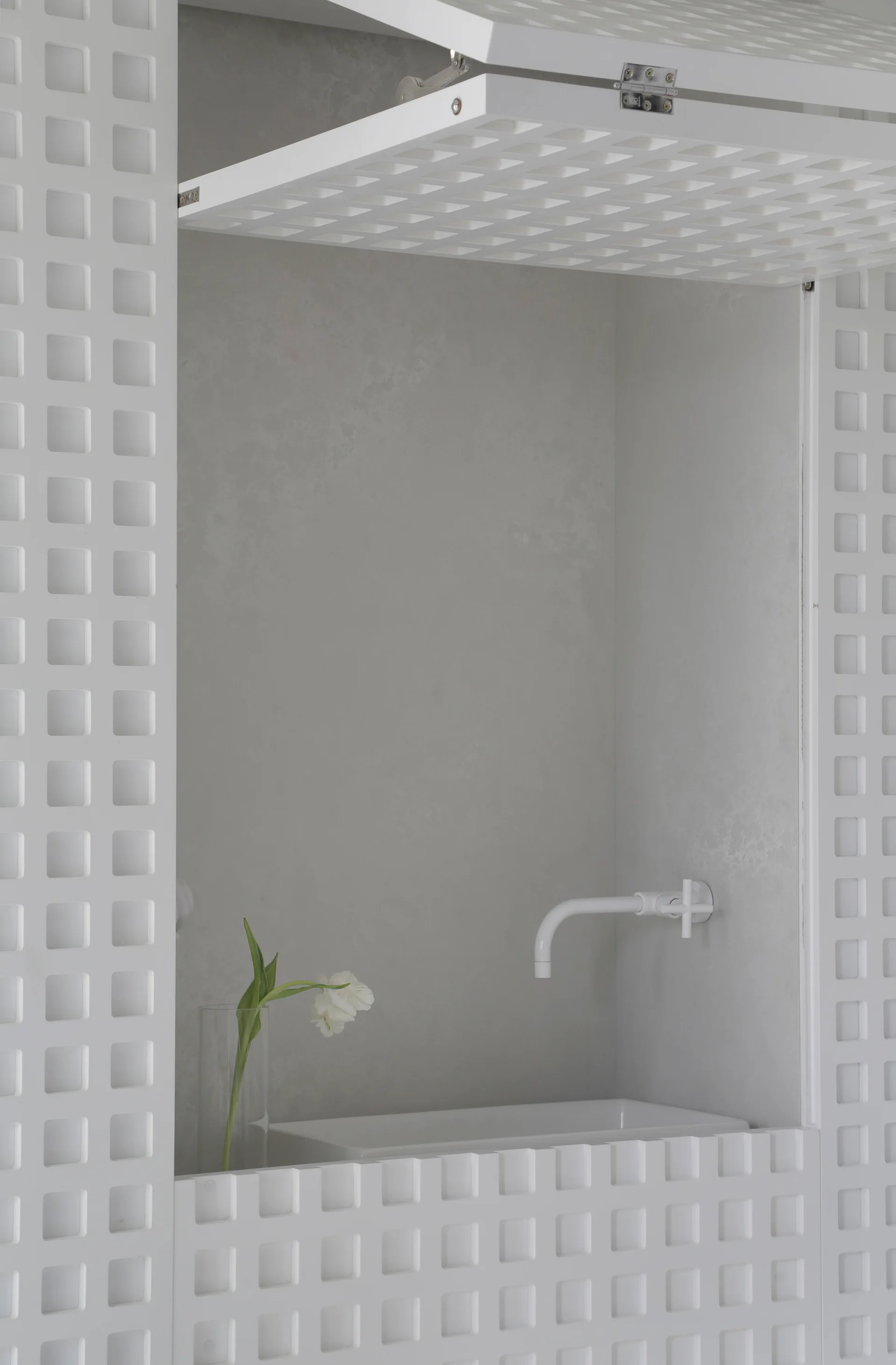 A white wall-mounted faucet and rectangular sink are recessed inside a smooth alcove surrounded by matching white grid-patterned cabinet doors.