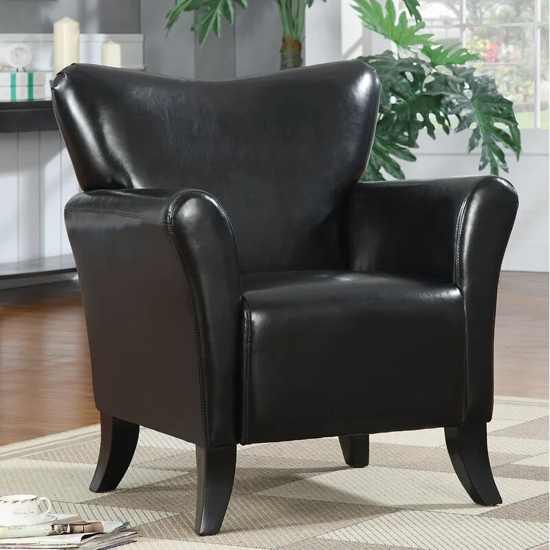 A black leather-like armchair with curved arms sits on a beige geometric patterned rug in front of a white wainscoted wall.