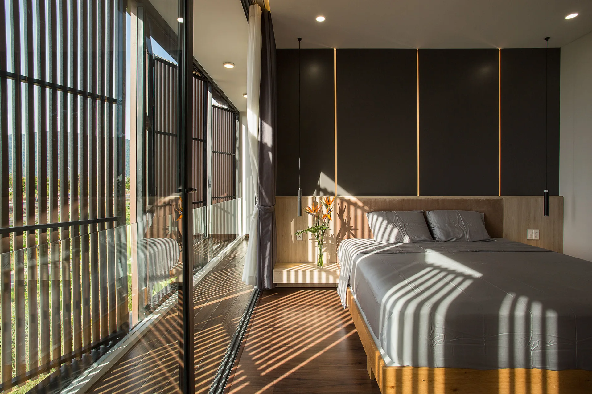 A contemporary bedroom features a bed with gray linens, an integrated headboard, and a sliding glass door with vertical wood louvers.