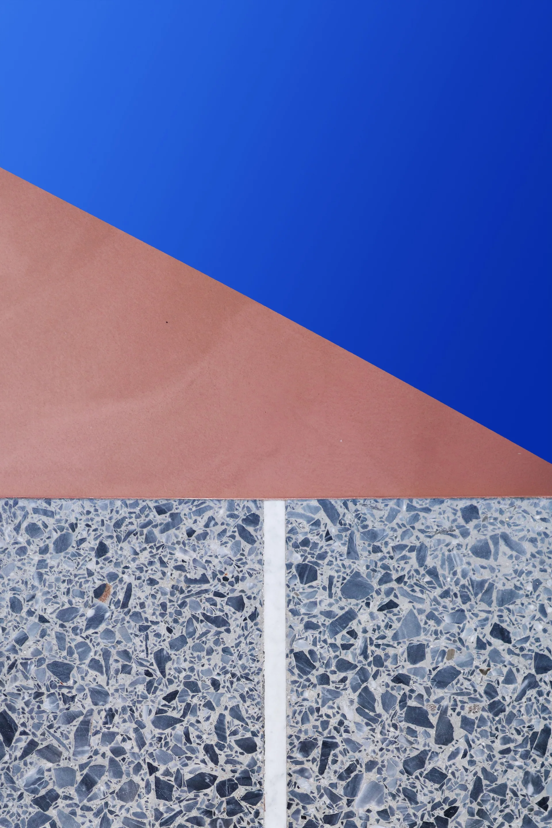 A close-up view of grey mottled terrazzo flooring split by a thin white marble inlay below diagonal sections of solid terracotta and deep cobalt blue.
