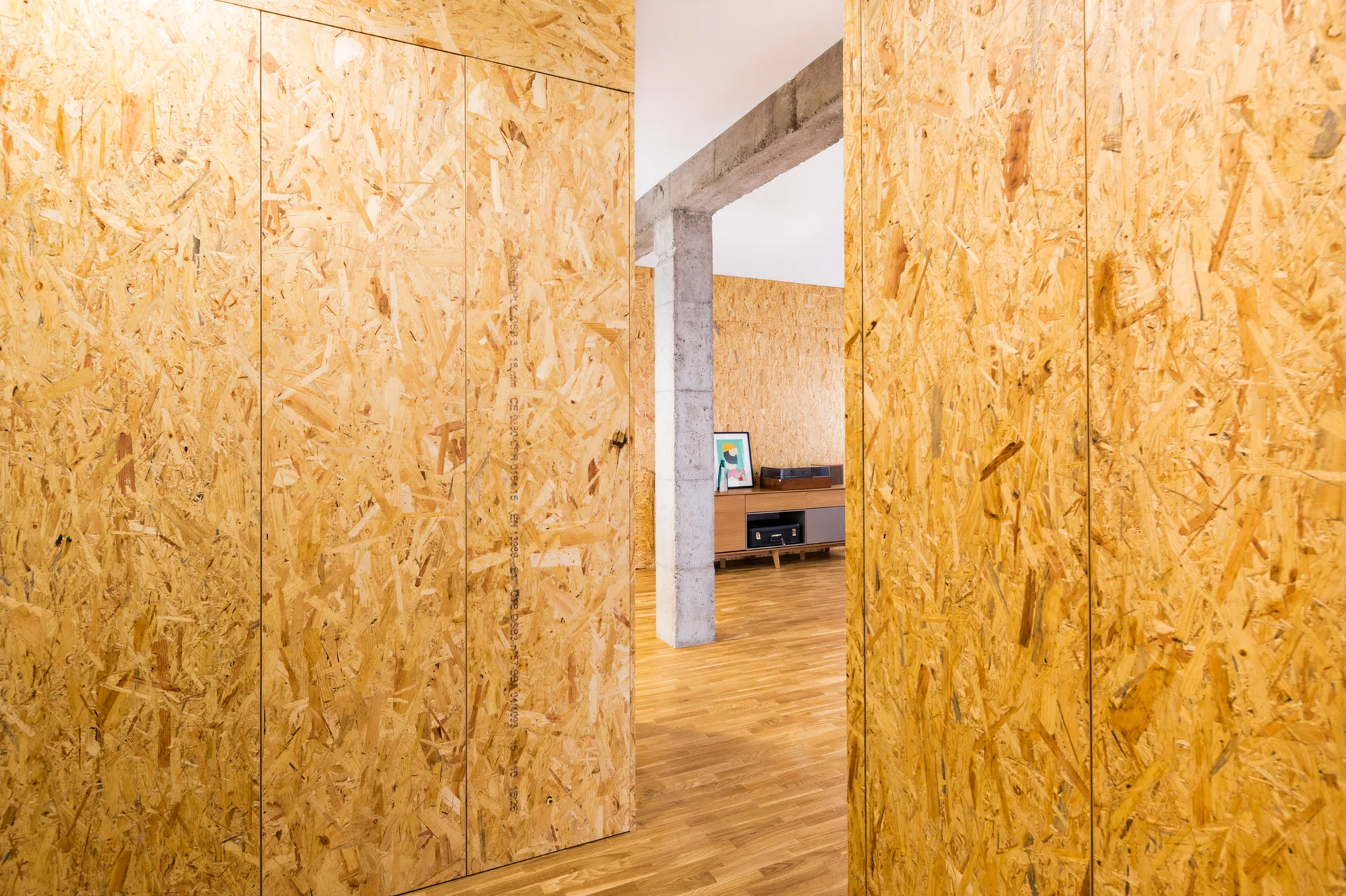An interior space featuring walls clad in oriented strand board panels next to a raw concrete structural column.