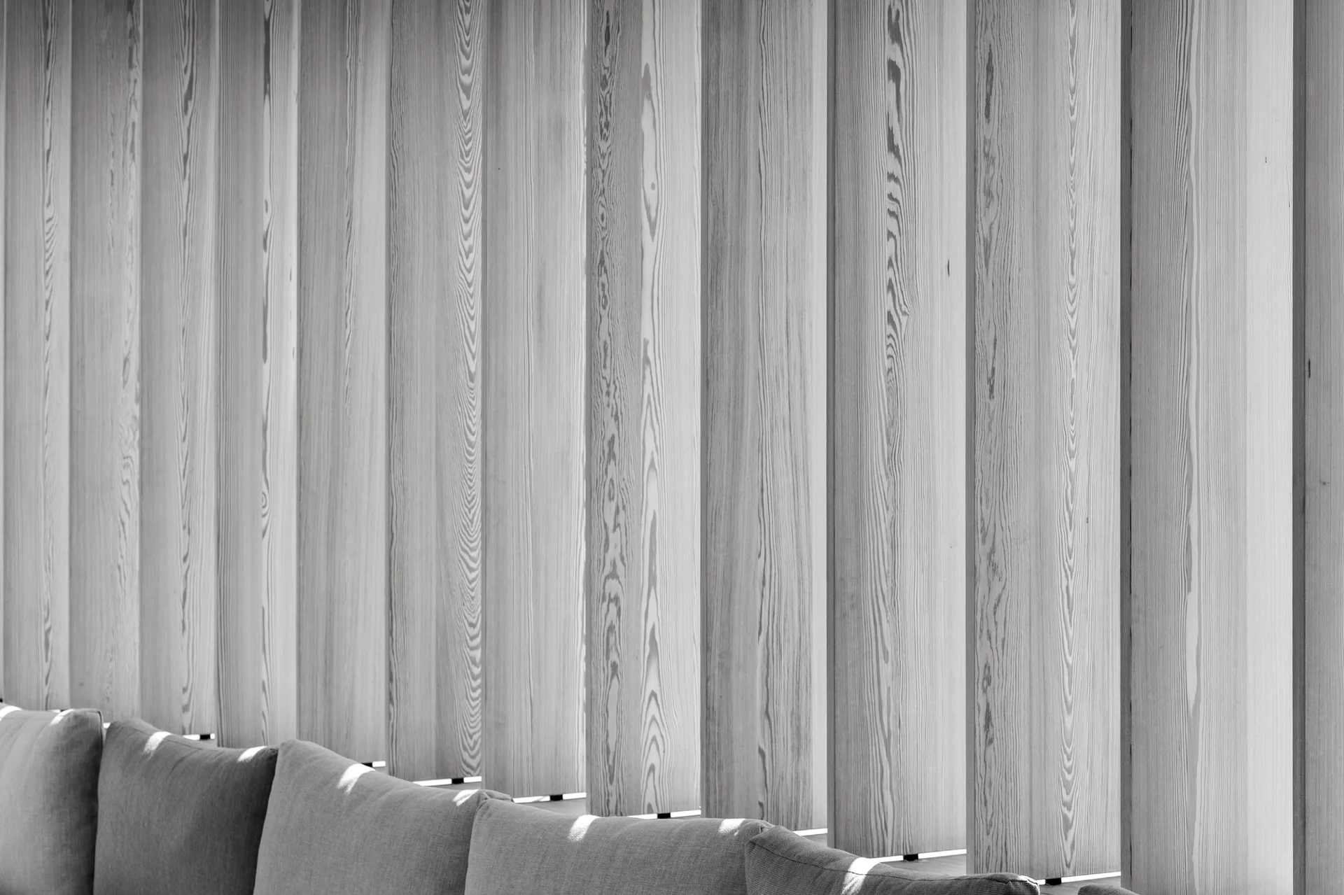 A close-up of vertical light wood panels with detailed grain patterns positioned behind a grey upholstered sofa.