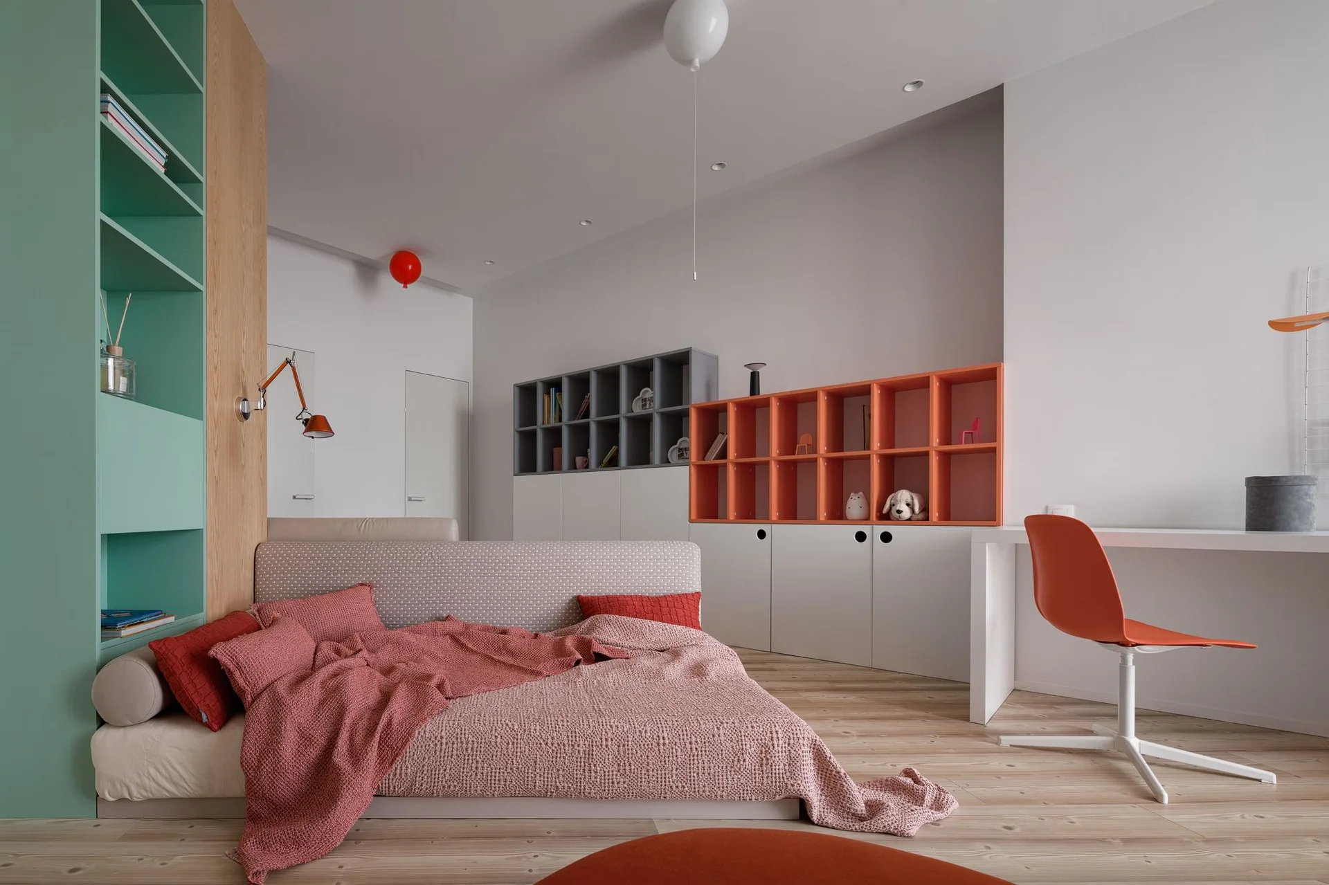 A minimalist bedroom features a low platform bed, light wood floors, a green built-in bookcase, and orange modular shelving with a white desk.