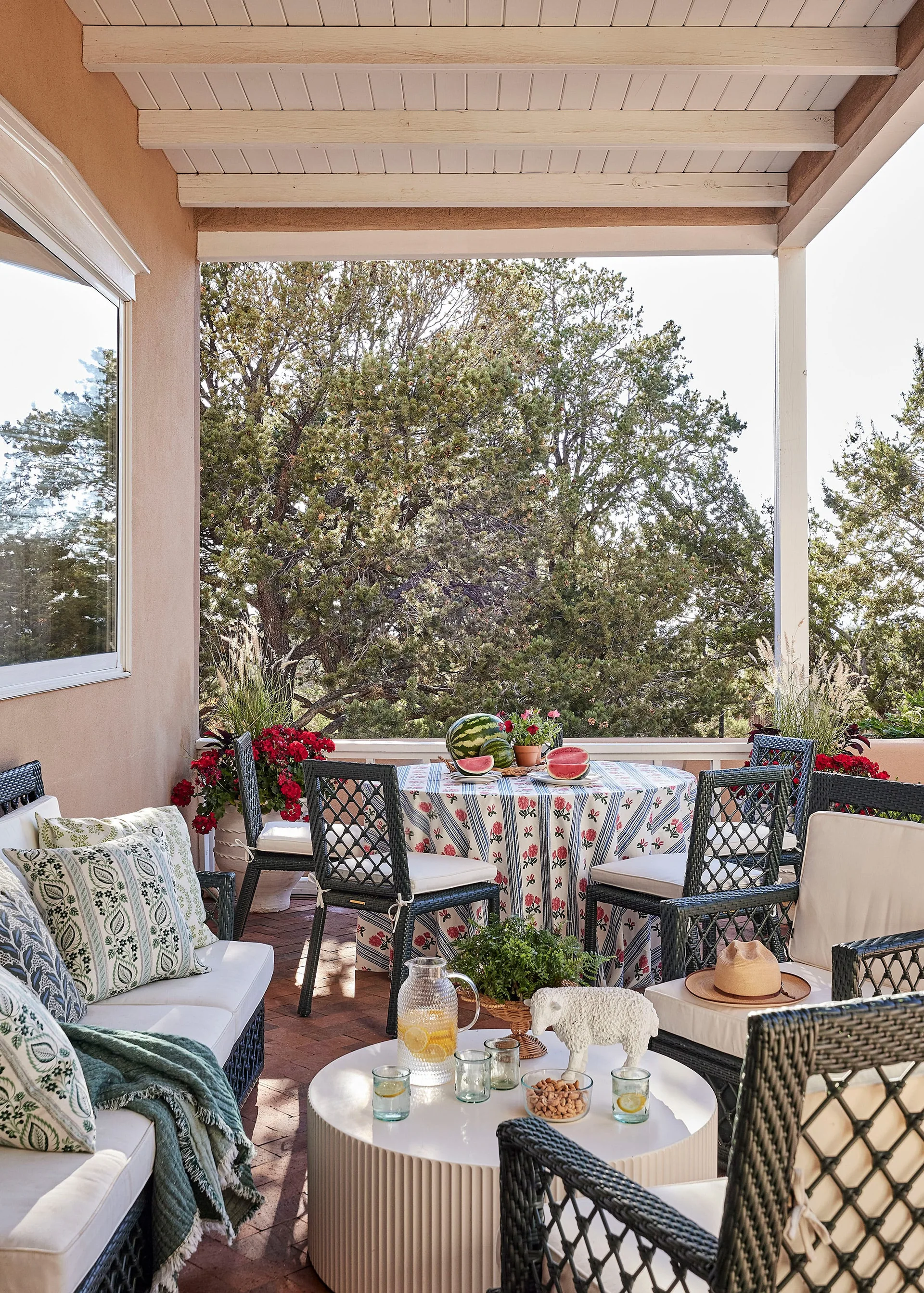 A covered outdoor patio features black wicker furniture with white cushions, a round dining table, and terracotta tile flooring.