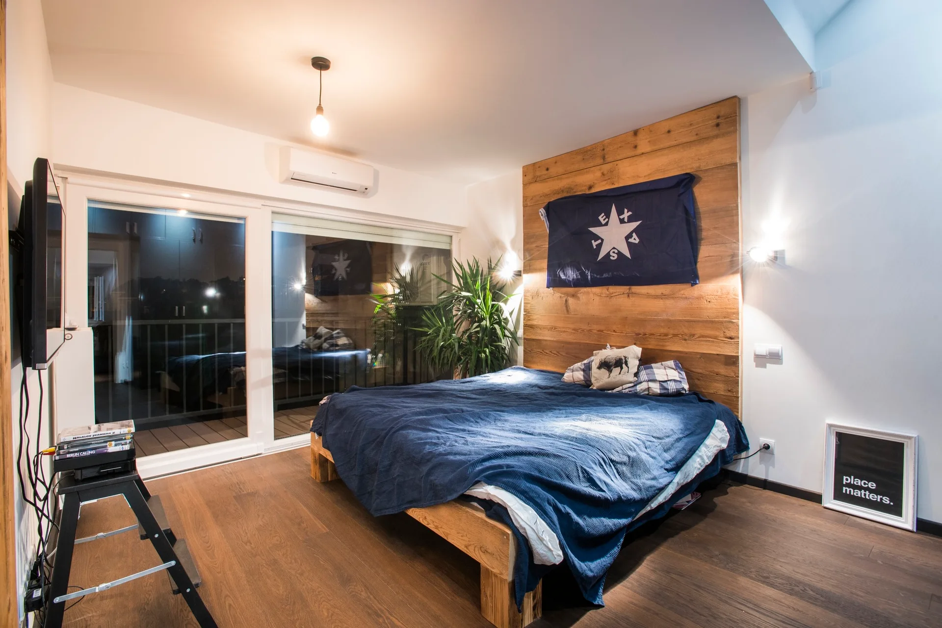 A modern bedroom featuring a wooden platform bed with blue bedding, a wood plank accent wall, and a sliding glass balcony door.