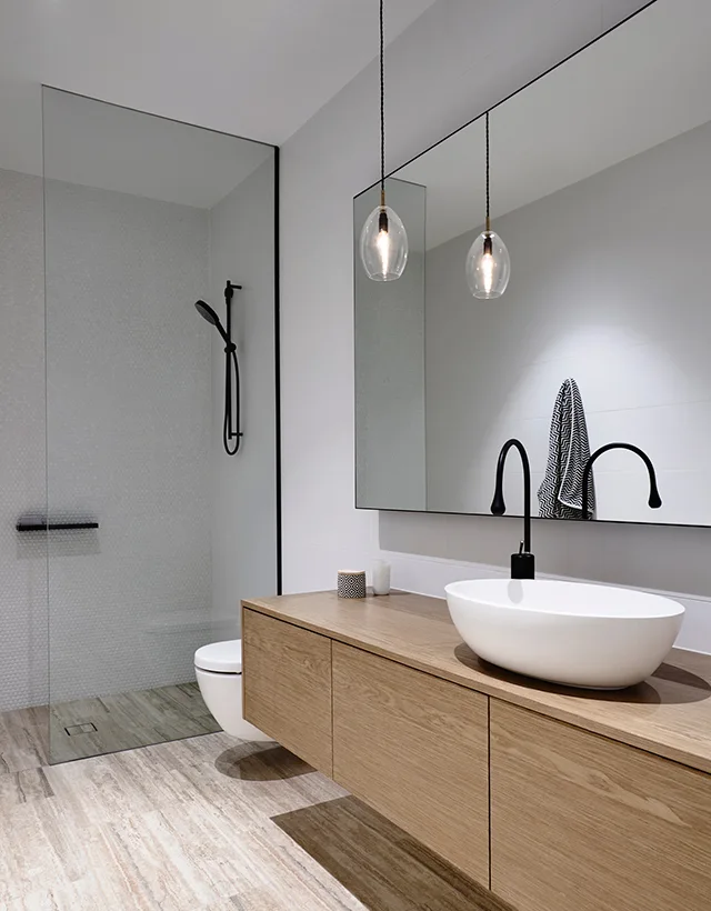 A modern bathroom features a floating wood vanity with a white vessel sink, matte black gooseneck faucet, and a frameless glass shower panel.