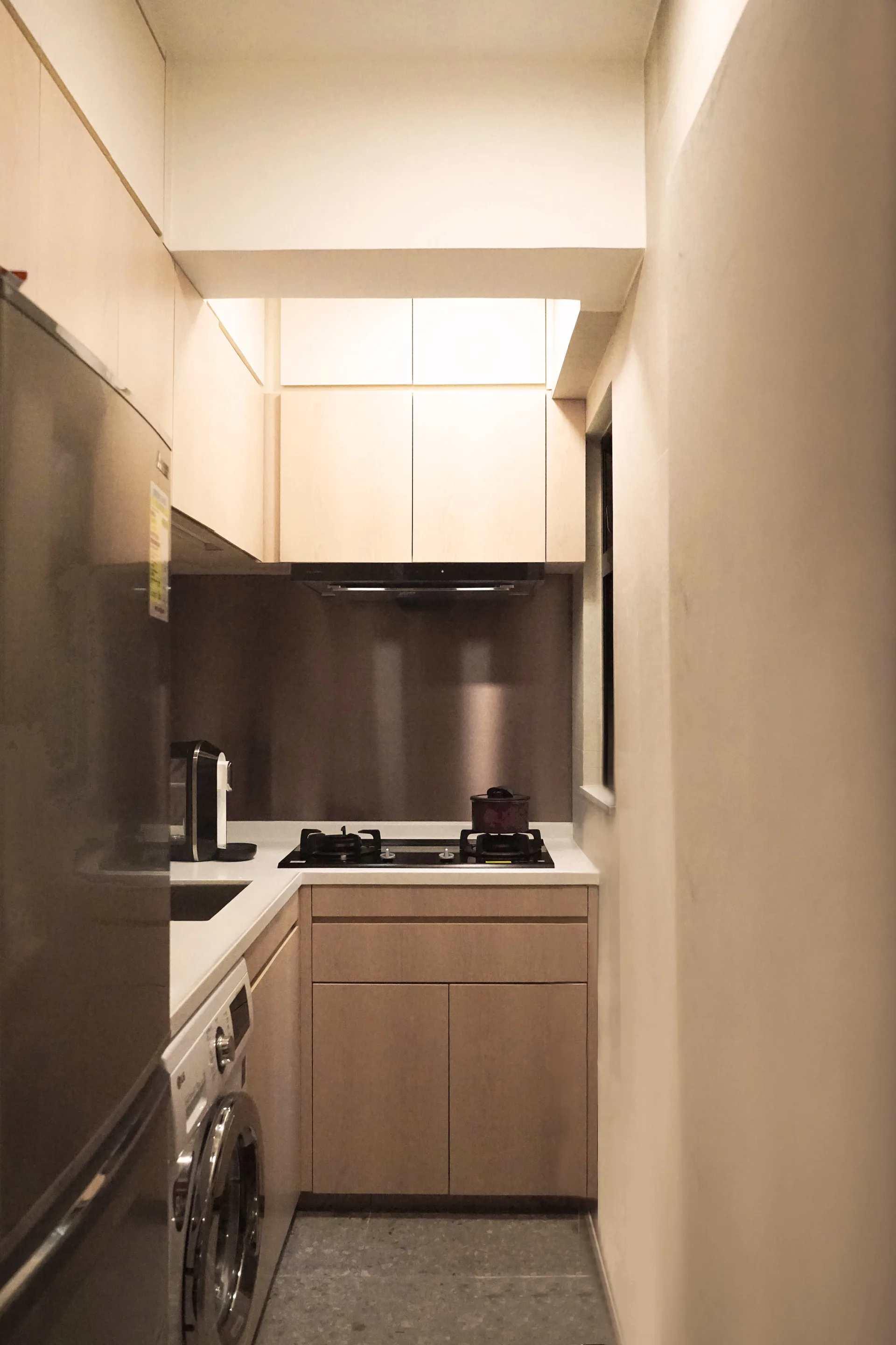 A compact galley kitchen features light wood cabinets, white countertops, and a washing machine integrated under the counter.
