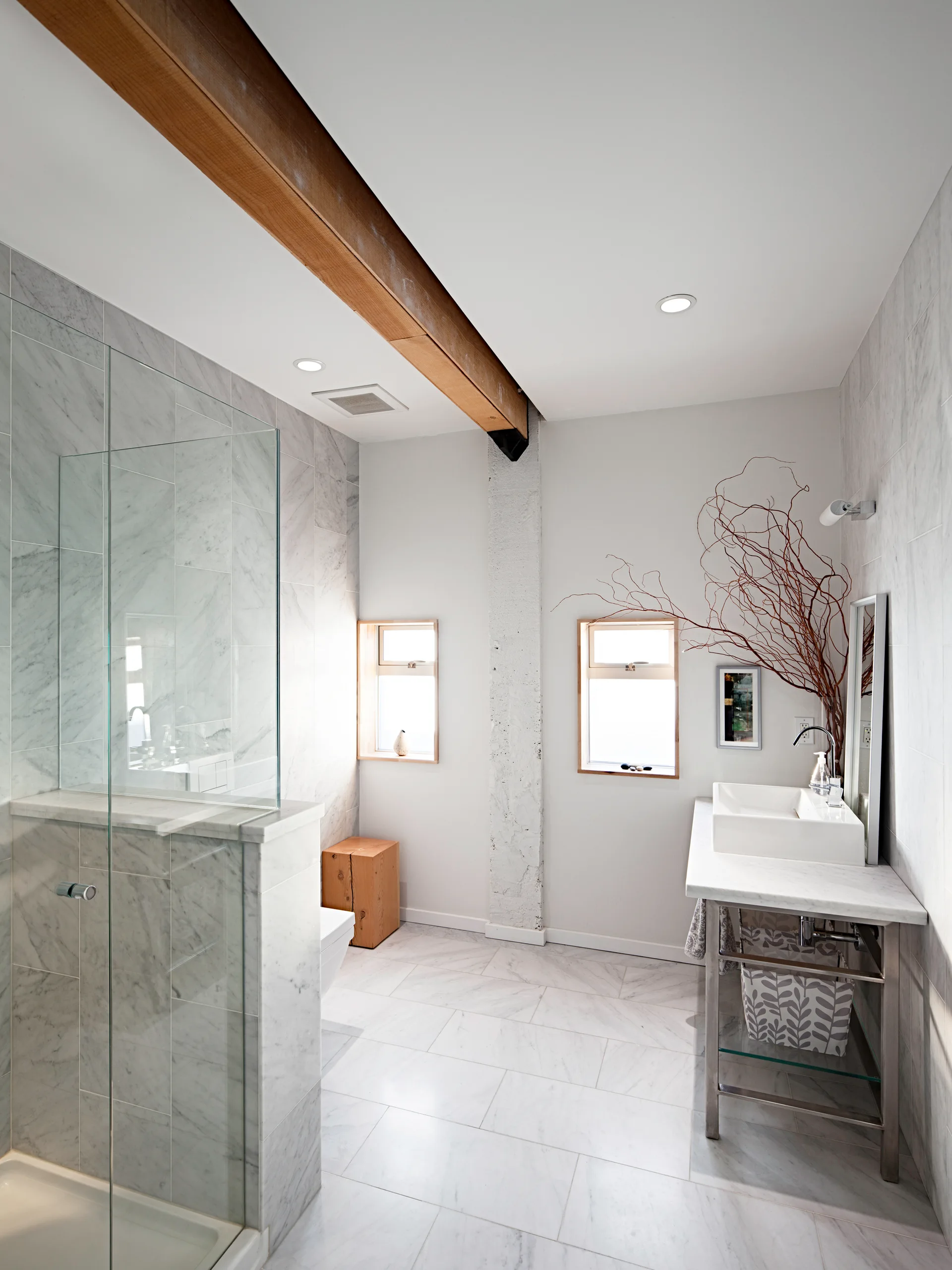 A bright modern bathroom featuring a marble-tiled walk-in shower, a metal console vanity, and an exposed wooden ceiling beam.