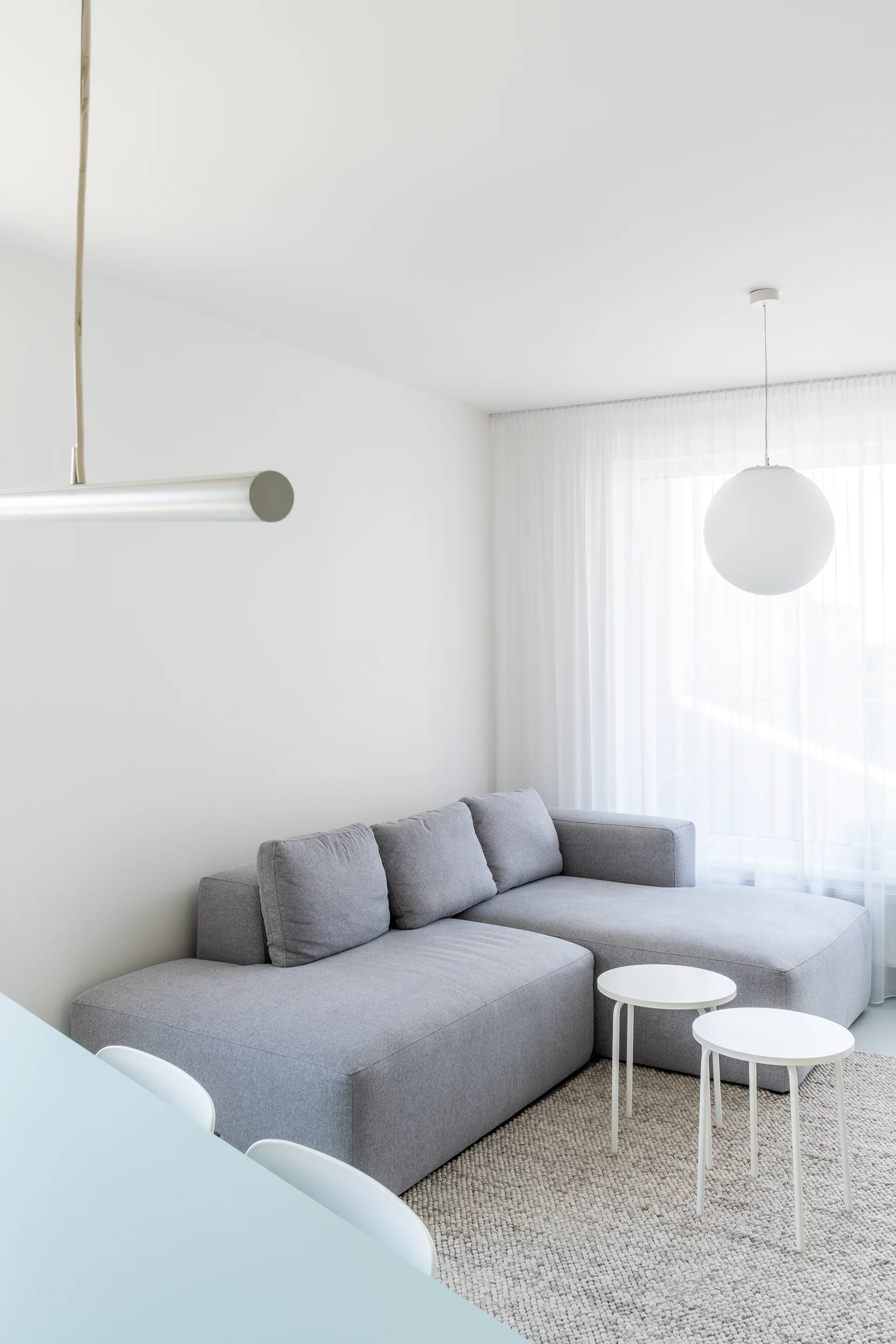 A minimalist white living room featuring a grey modular sectional sofa, two small round side tables, and a textured loop area rug.