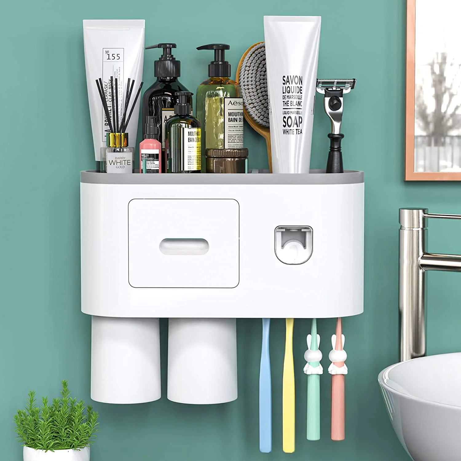 A white wall-mounted bathroom organizer holding various toiletries and colorful toothbrushes against a teal green wall next to a sink.