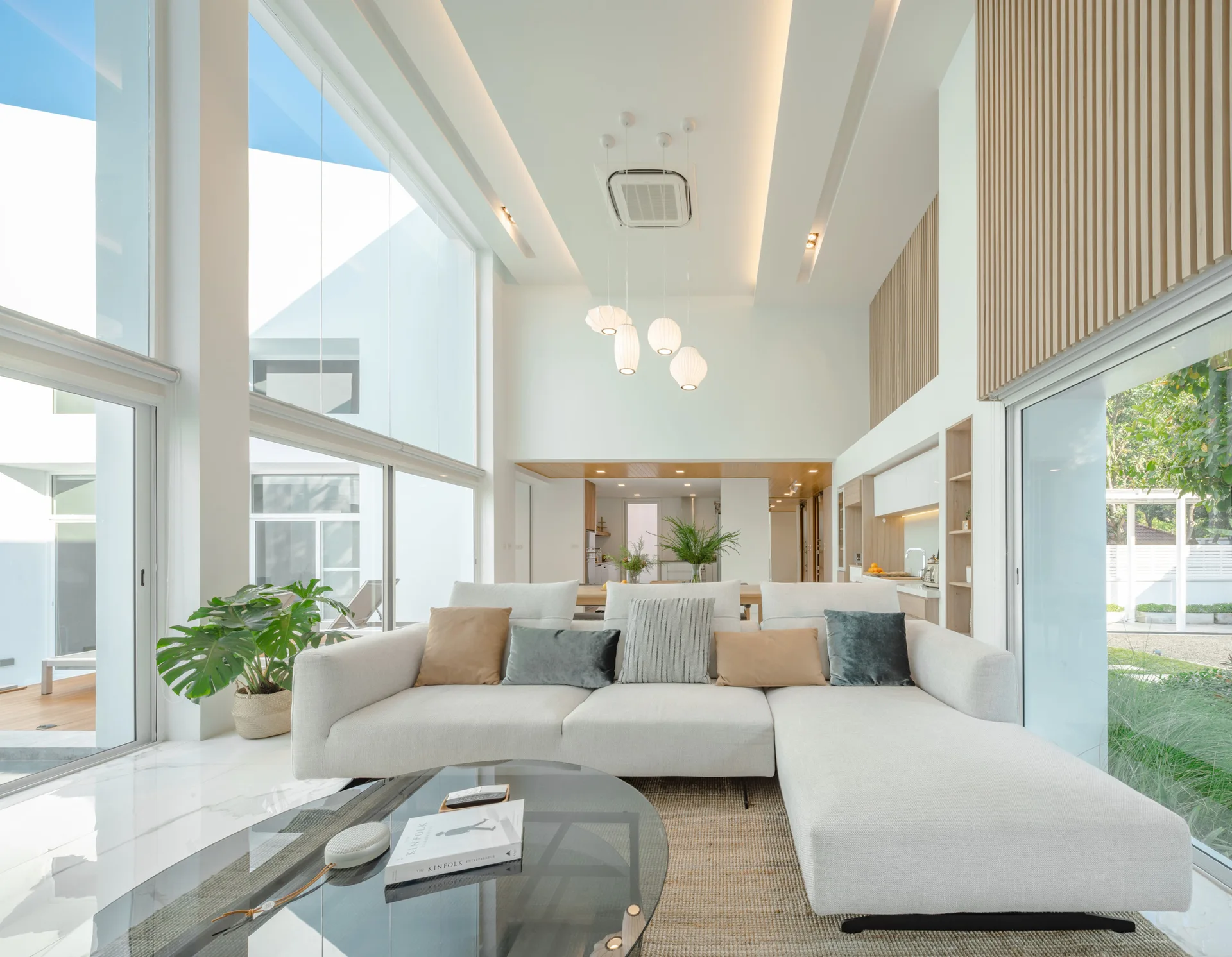 A modern double-height living room features a cream sectional, vertical wood slat wall panels, and large floor-to-ceiling windows.