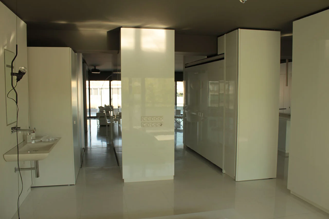 A minimalist bathroom and hallway area with glossy white partition cabinets, a wall-mounted ceramic sink, and a dark gray painted ceiling.