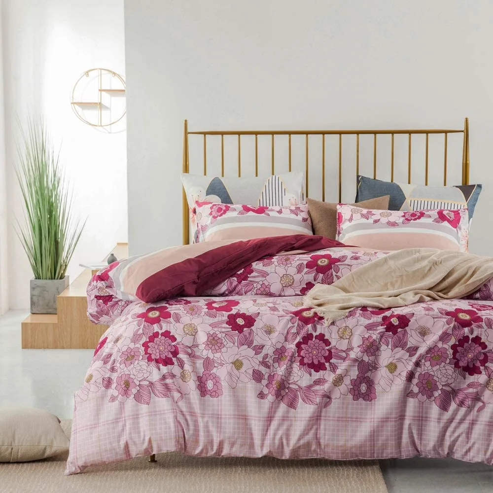 A contemporary bed features pink and burgundy floral patterned bedding and a gold metal spindle headboard against white walls.