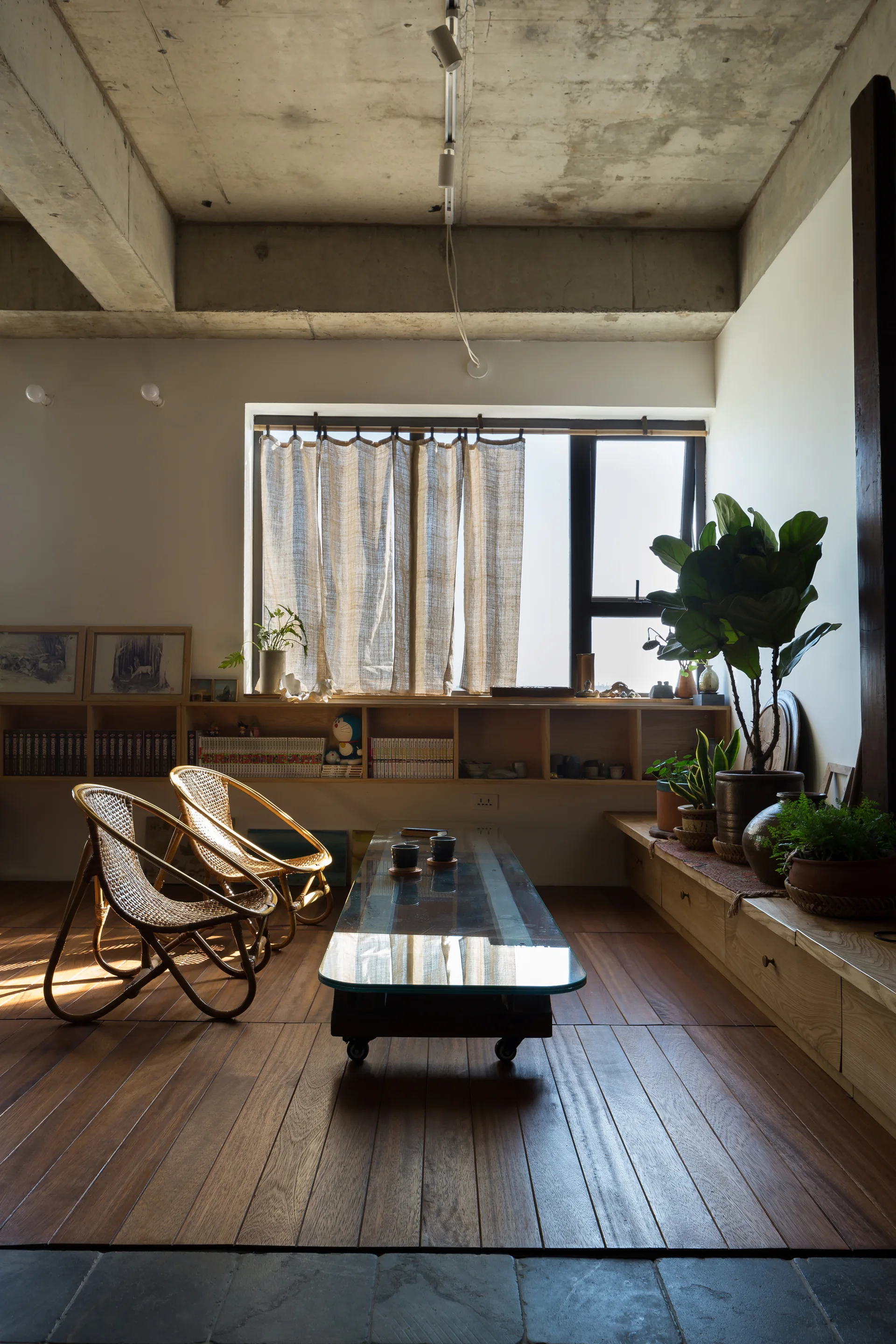 A minimalist living room with two curved rattan chairs, a low glass-topped coffee table, and an exposed concrete ceiling.