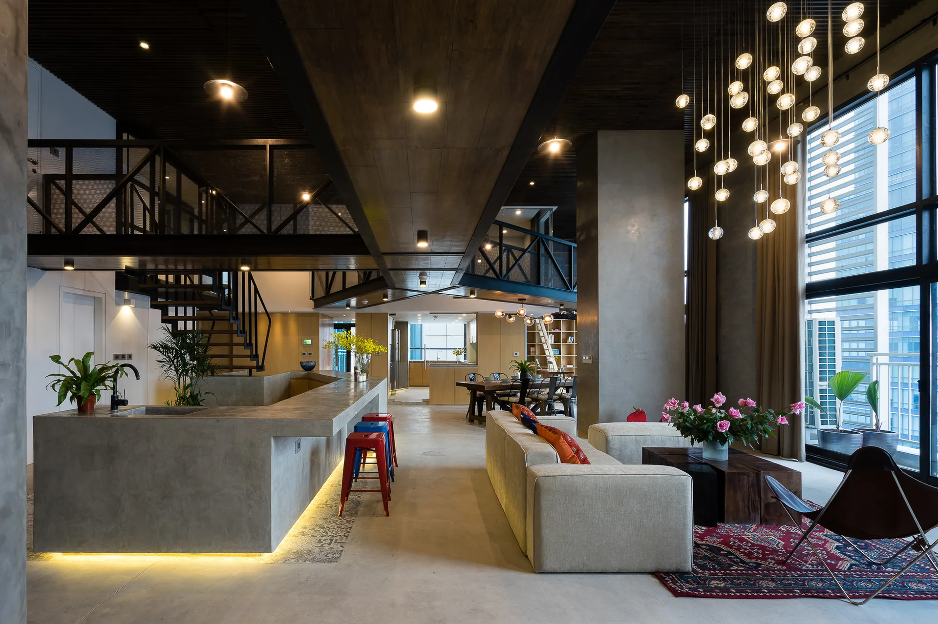 An industrial open-plan living space features a large concrete kitchen island, a cream sectional sofa, a dark wooden slatted ceiling, and an upper mezzanine.