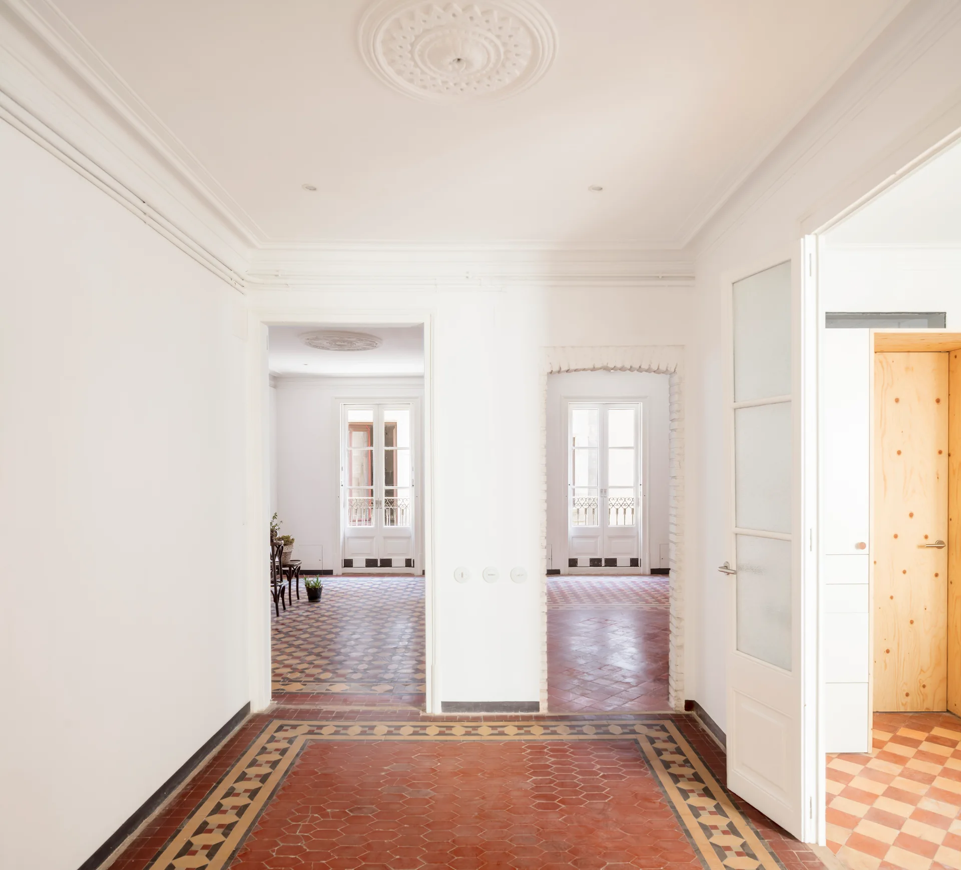 A bright white hallway features patterned terracotta tile floors, a decorative ceiling medallion, and an exposed brick archway leading to adjacent rooms.