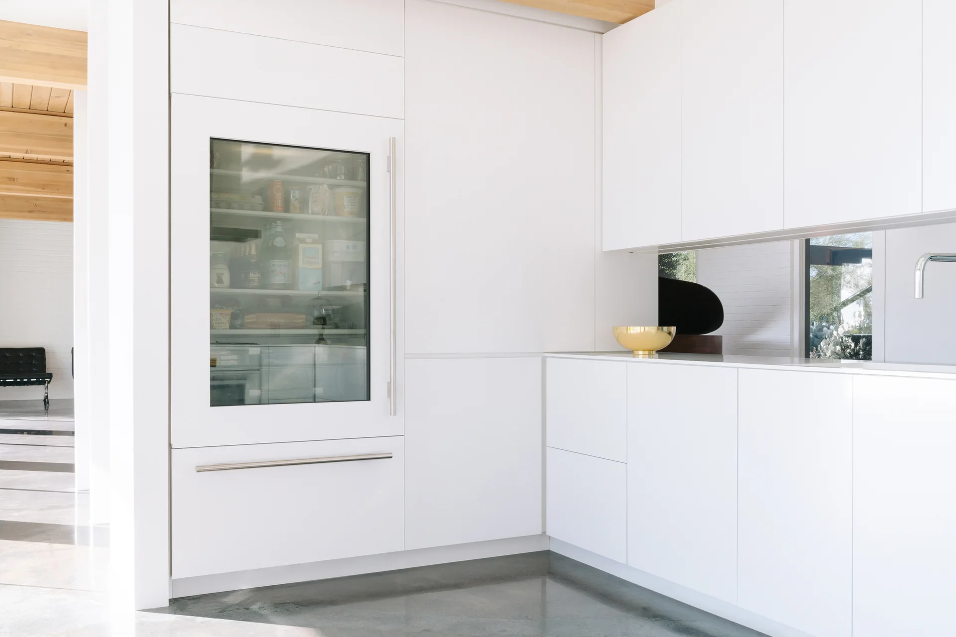 A minimalist white kitchen featuring flat-front cabinetry, an integrated glass-door refrigerator, and a polished concrete floor.