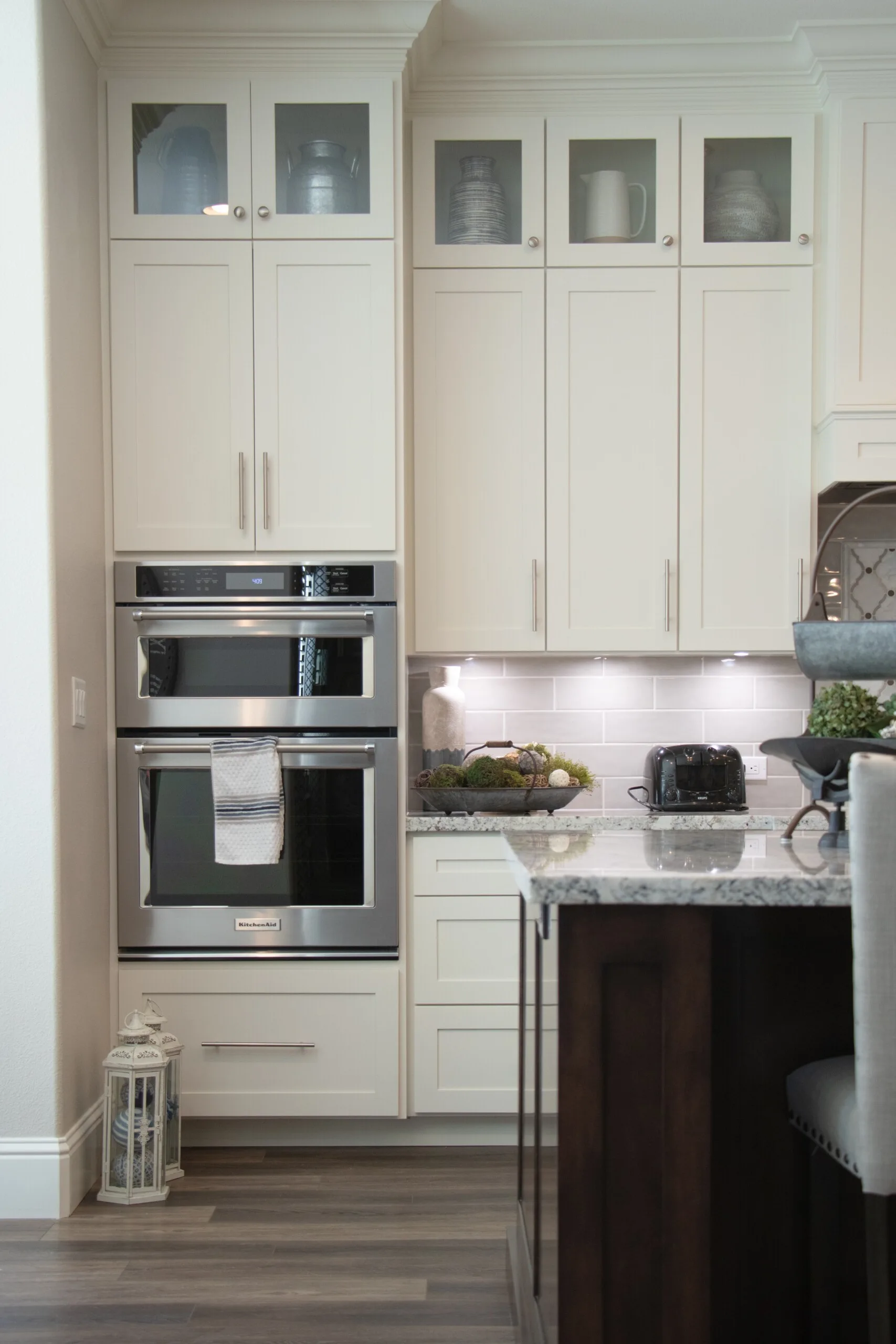 A kitchen featuring off-white shaker cabinets, a built-in stainless steel double oven, and a granite-topped island.