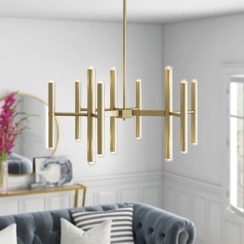 A modern brushed brass multi-arm chandelier hangs in a living room featuring a blue tufted sofa and white wainscoted walls.