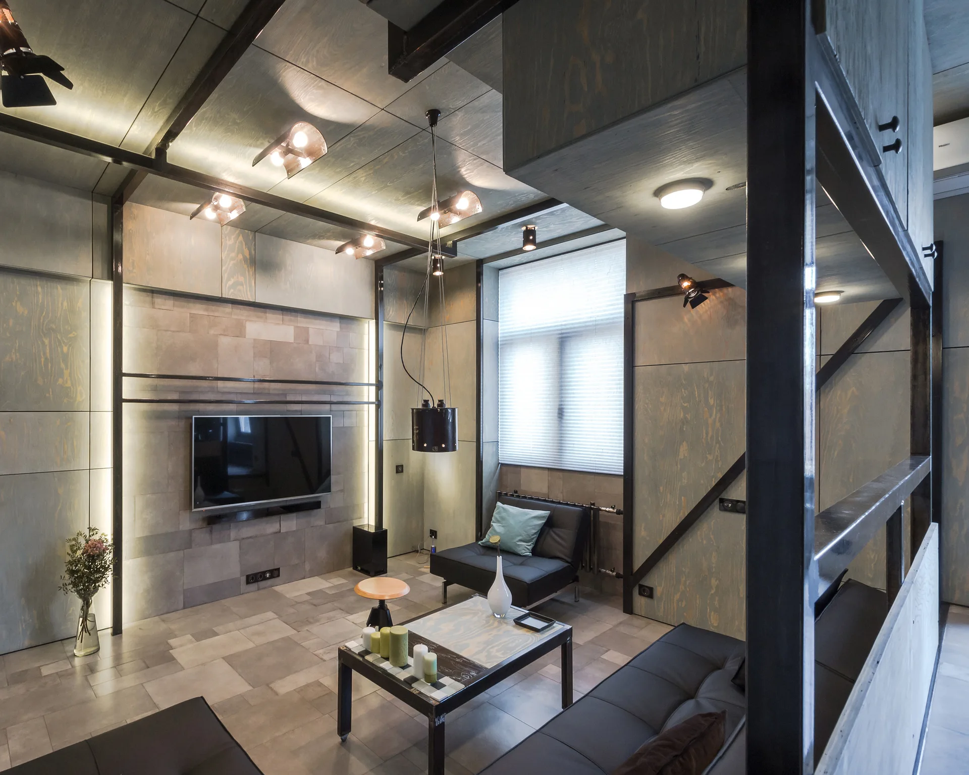 An industrial living room features stained plywood wall paneling, a stone-tiled media wall with a TV, black leather sofas, and exposed steel beams.