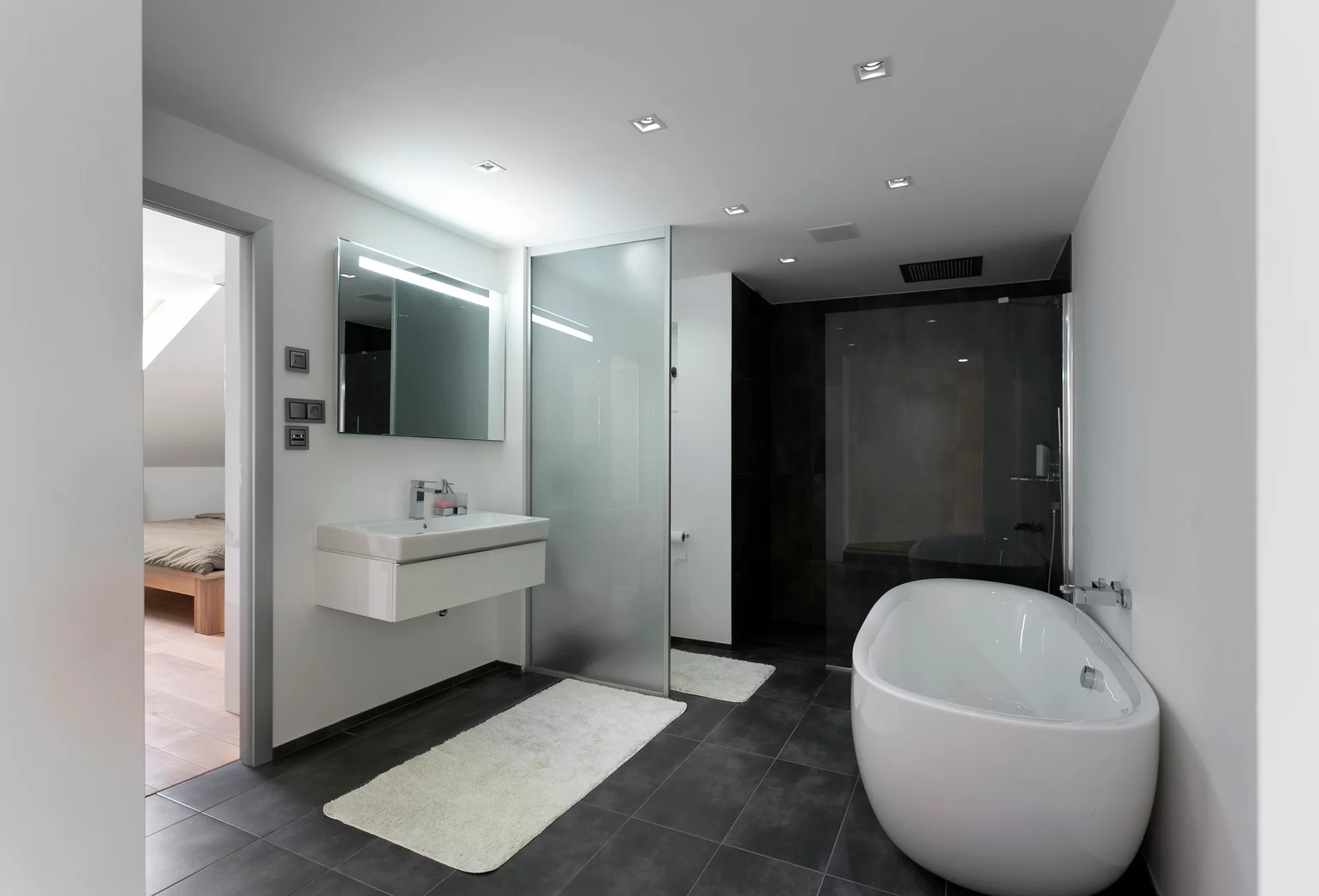 A modern minimalist bathroom featuring a white freestanding bathtub, a floating vanity, and dark gray floor tiles.