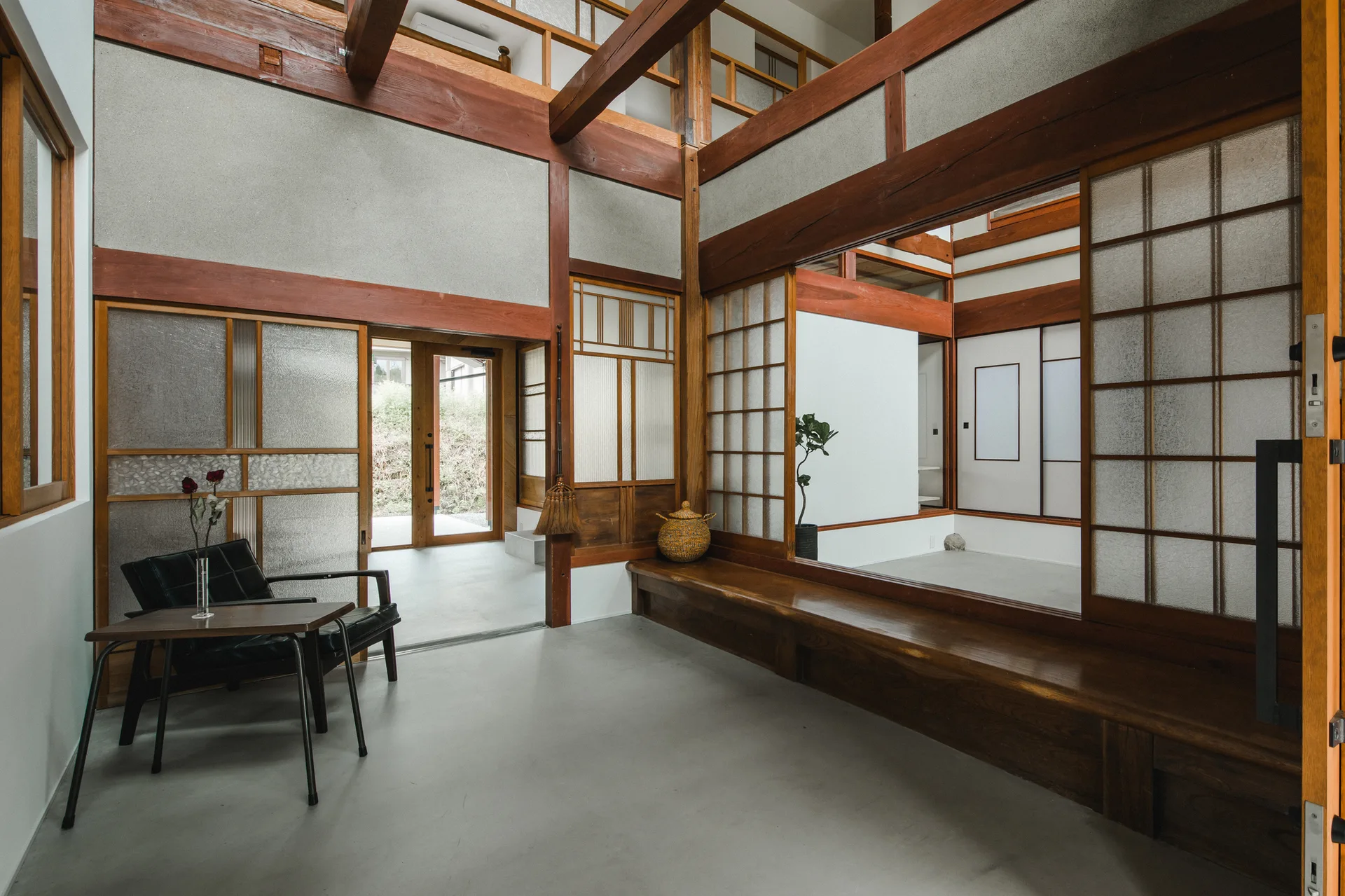 A spacious Japanese style entryway features exposed timber beams, sliding shoji screens, a concrete floor, and a long built-in wooden bench.