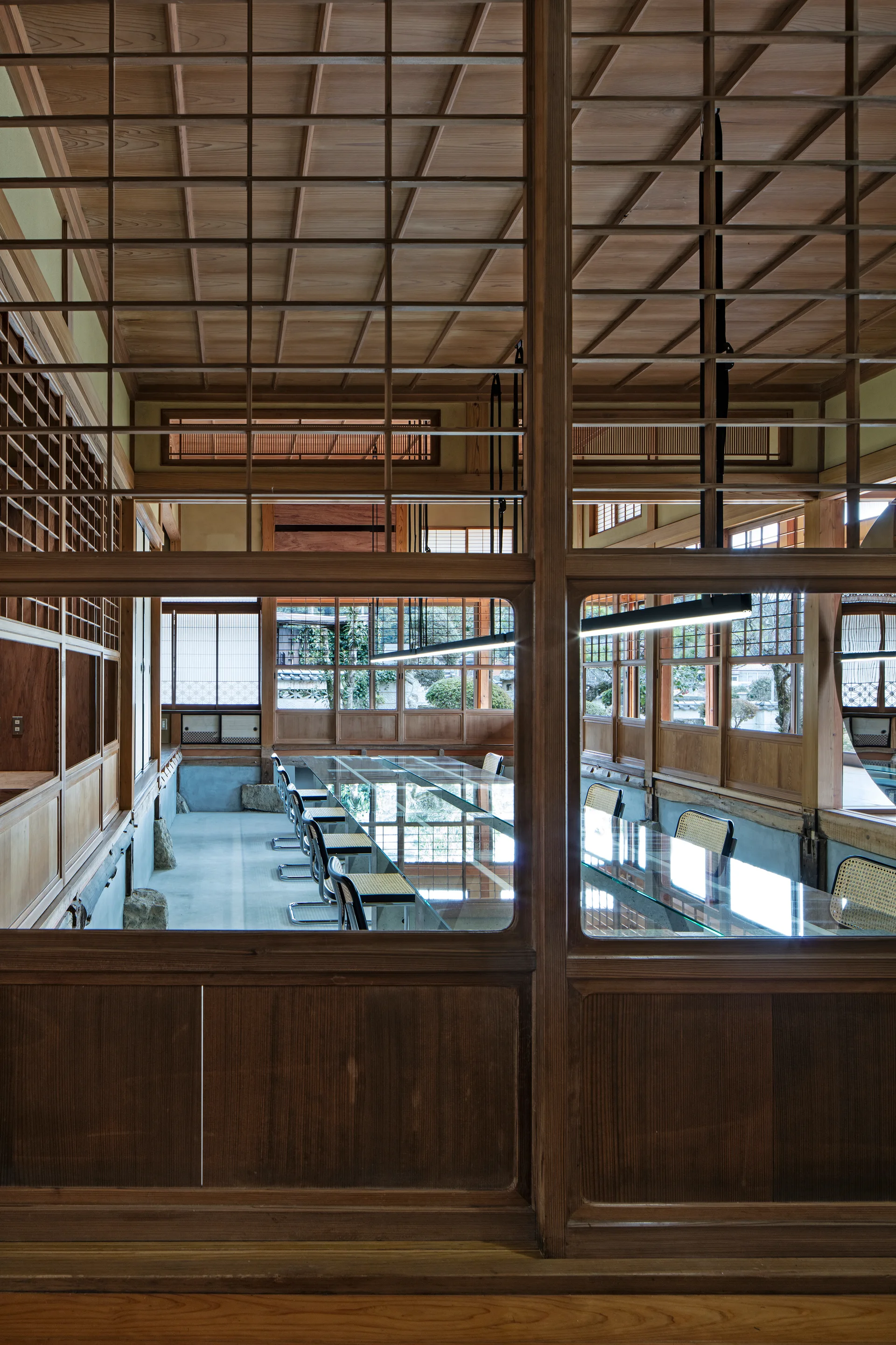 A long glass conference table with cane chairs is set in a room featuring traditional Japanese wood grid sliding doors and a paneled ceiling.