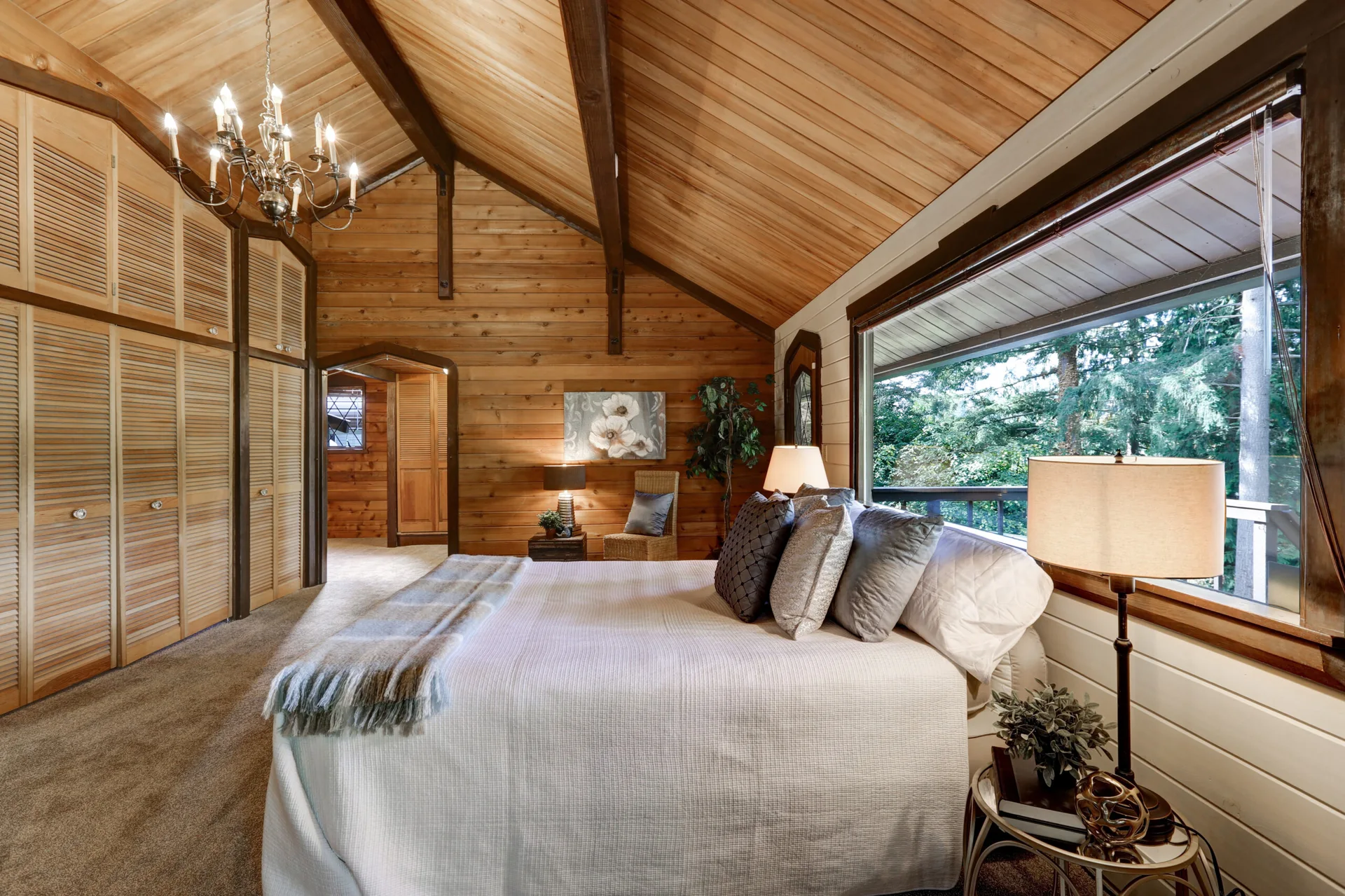 A rustic bedroom featuring a high vaulted wood ceiling with beams, a bed with white linens, and a wall of built-in louvered wood closets.