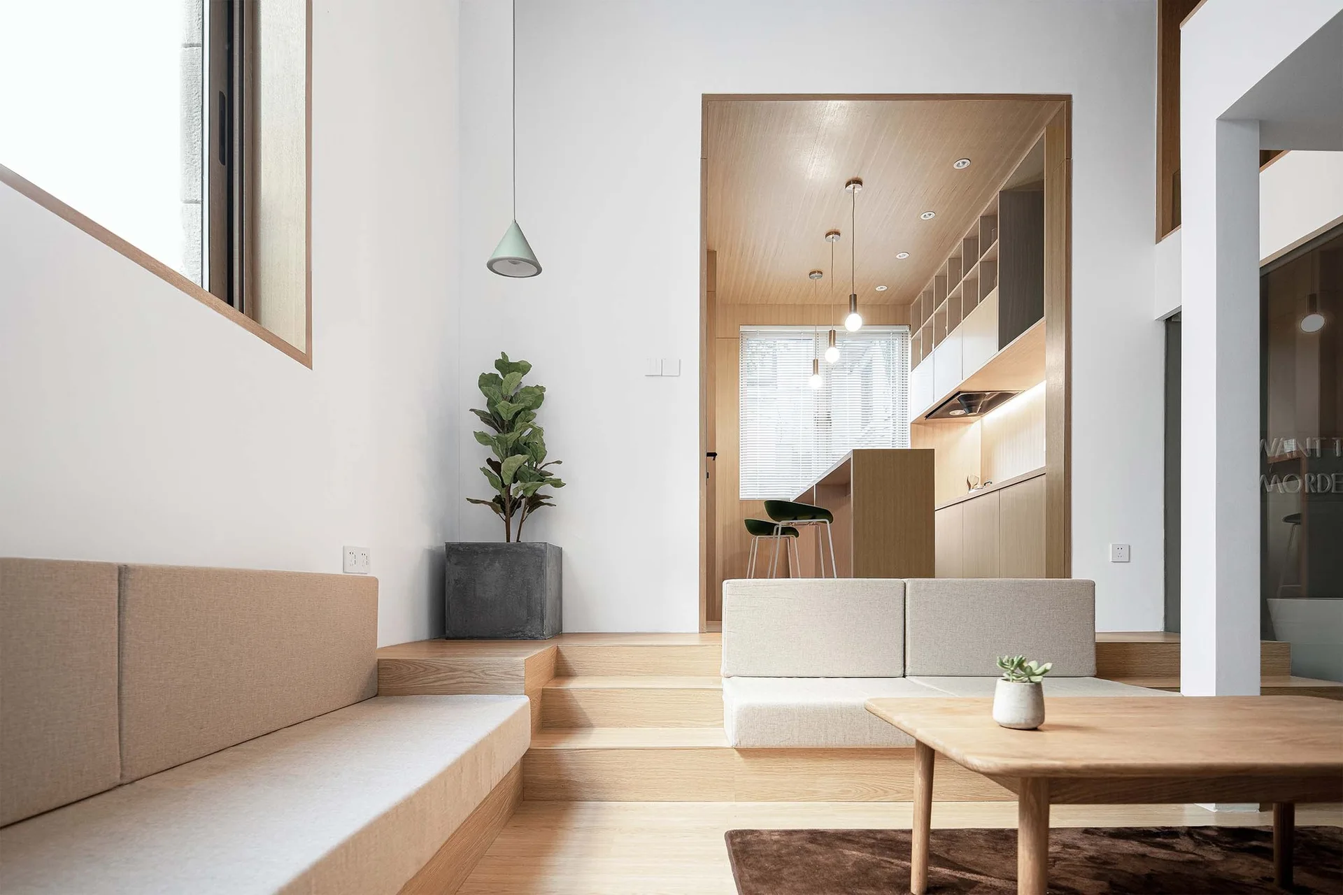 A modern sunken living room features a stepped wooden platform leading to a wood-lined kitchen, built-in beige sofas, and a wooden coffee table.