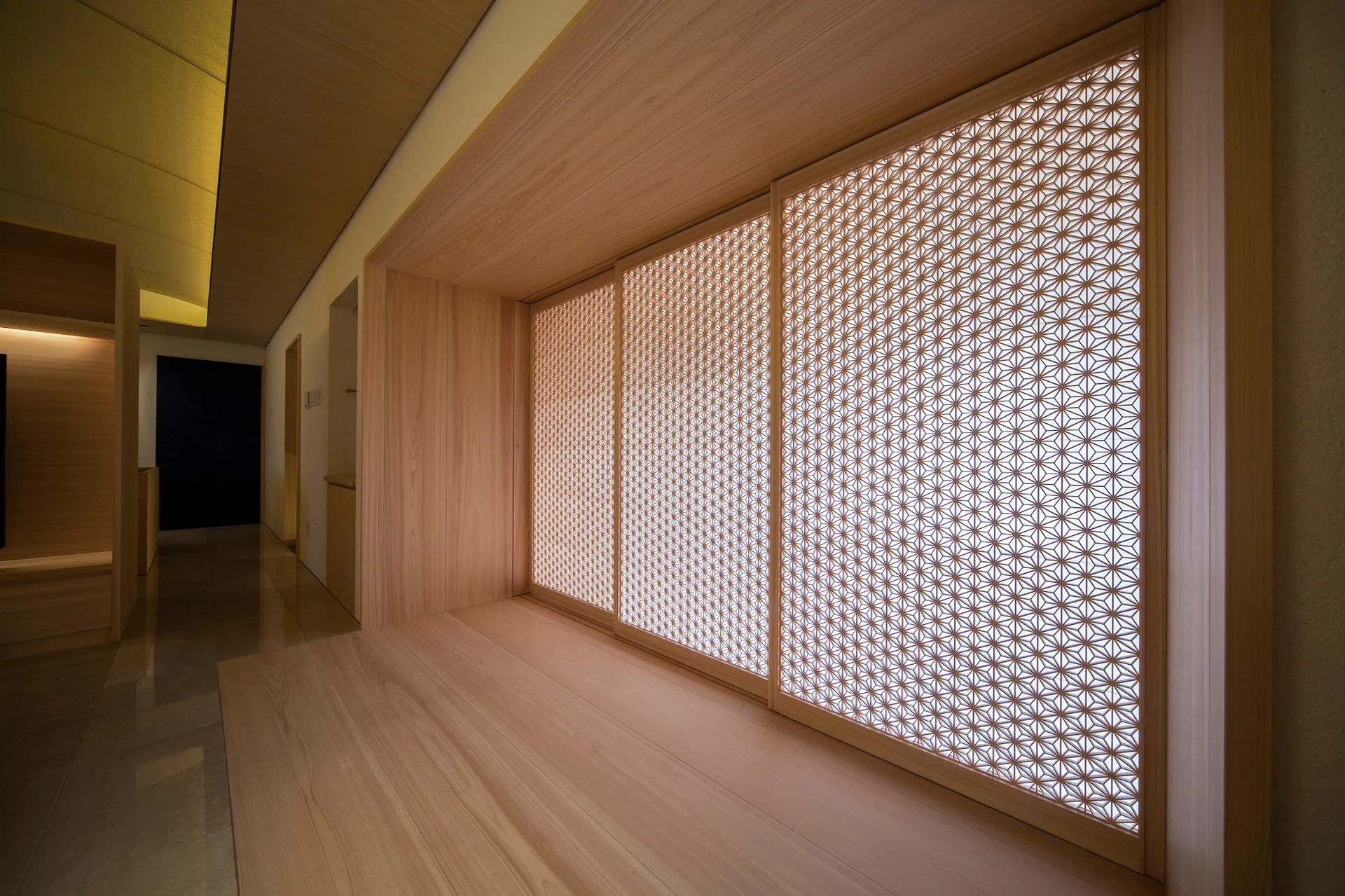 An interior corridor features backlit sliding shoji screens with intricate wood geometric lattice work set within a light-colored wooden recess.