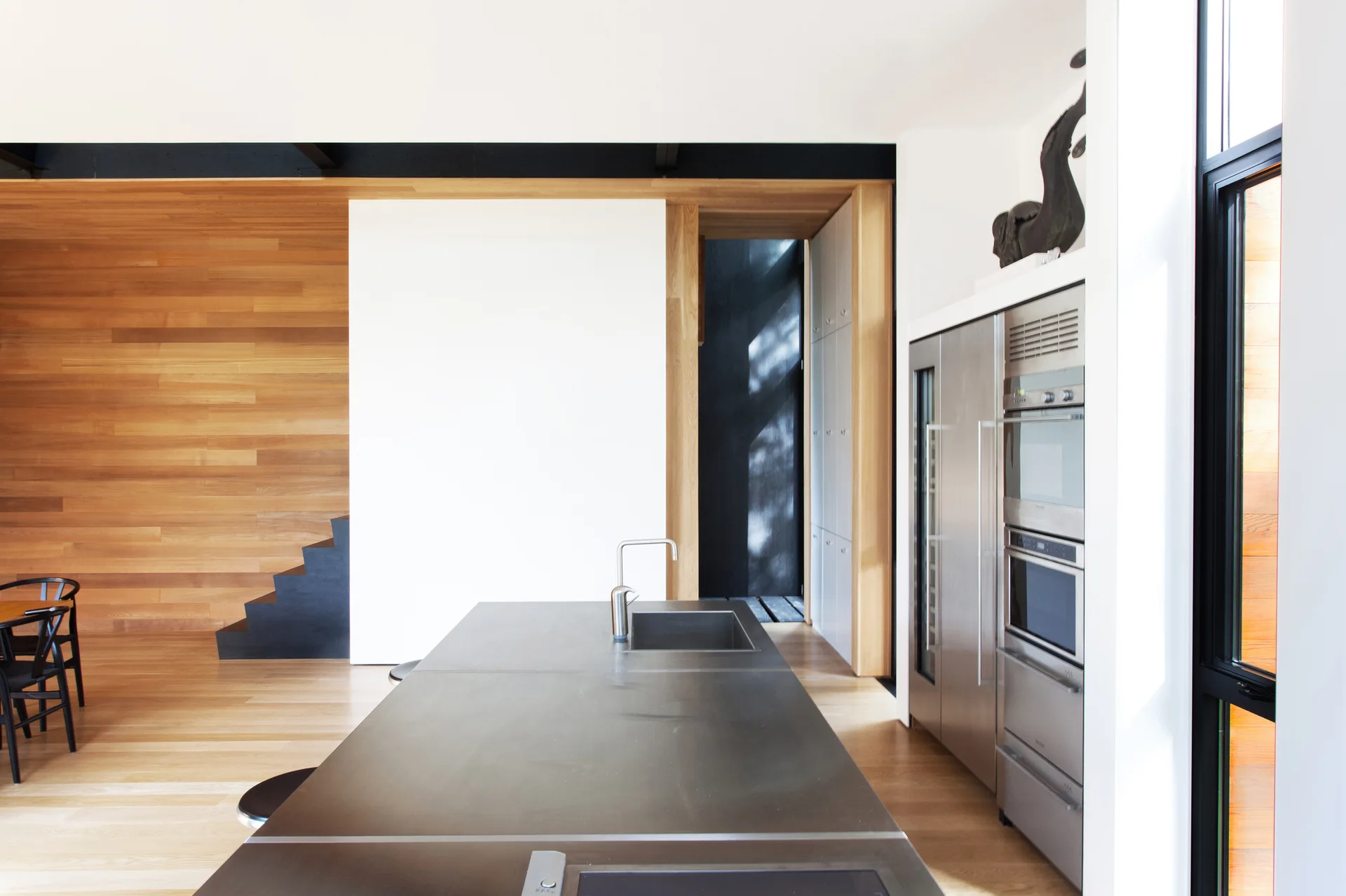 A minimalist kitchen features a stainless steel island with a sink, built-in appliances, and warm horizontal wood-paneled walls.
