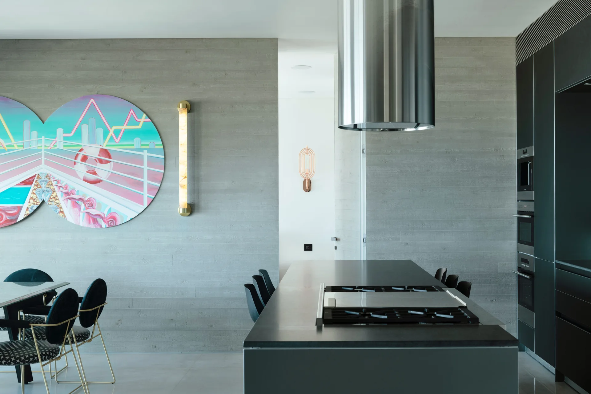 A modern kitchen with a dark grey island, a cylindrical range hood, and a textured wood-plank wall featuring a colorful circular painting.