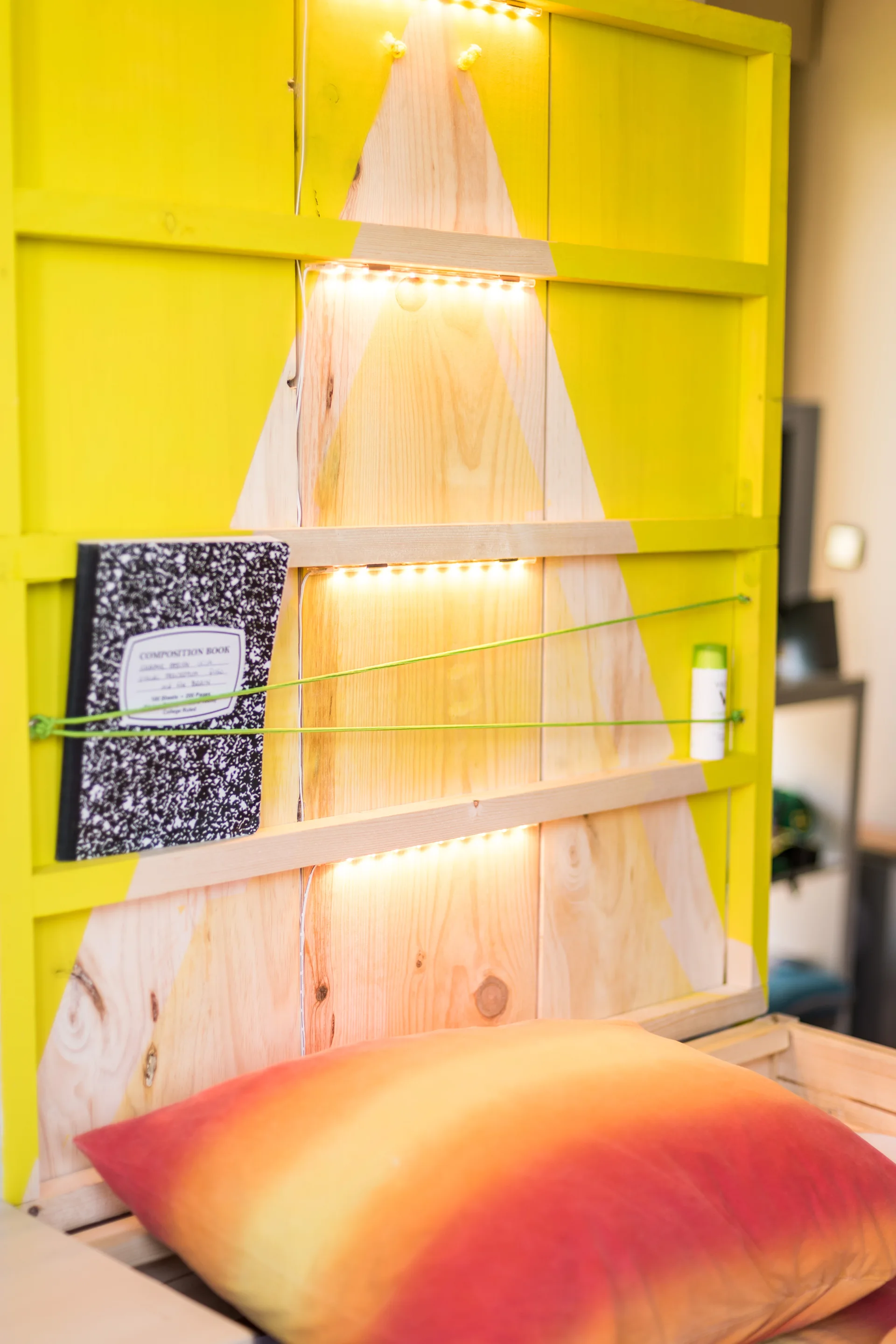 A custom wooden headboard painted bright yellow with natural pine accents, featuring integrated LED light strips and an ombre patterned pillow.