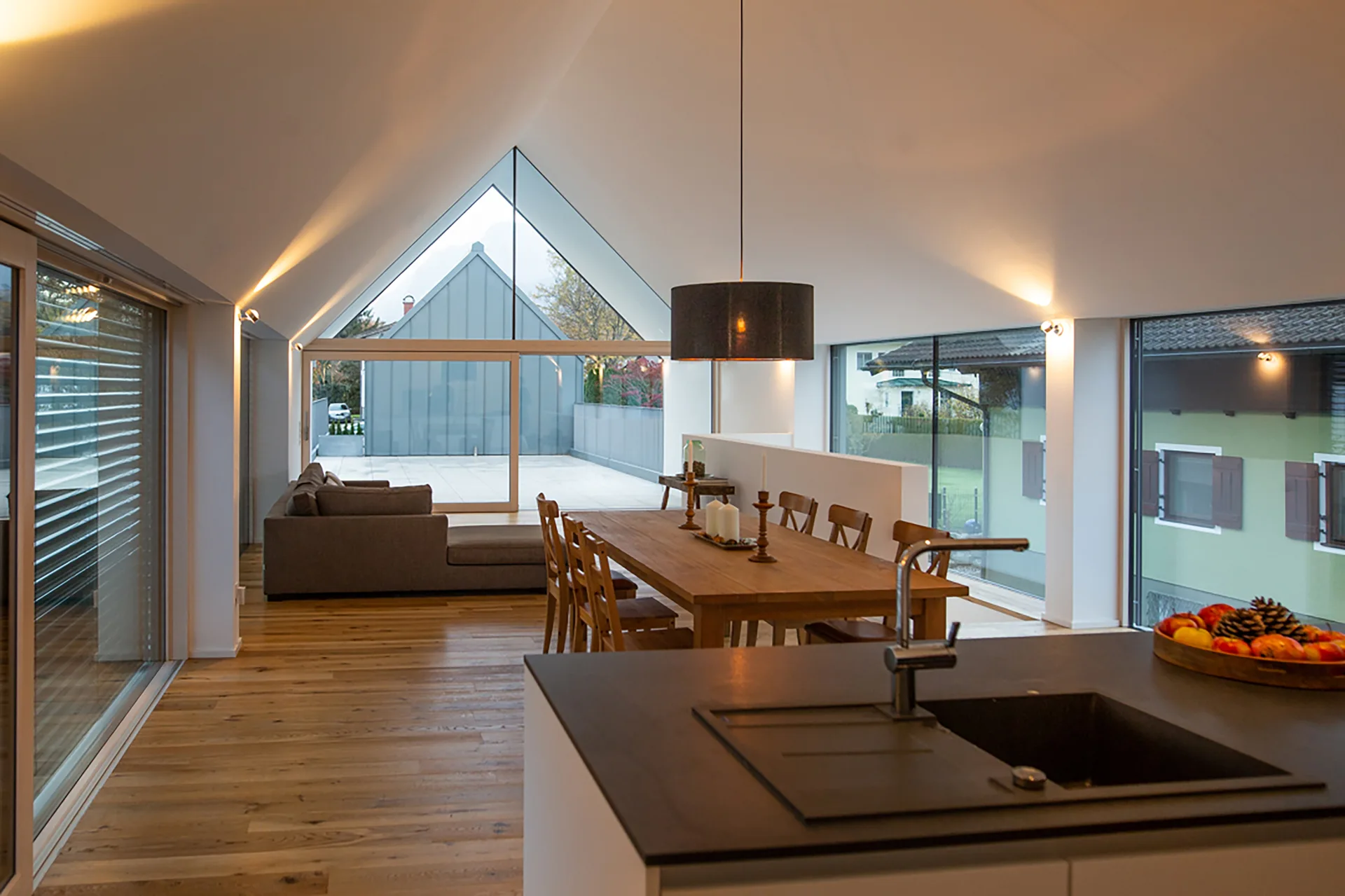 A modern open-plan home featuring a white vaulted ceiling, a wooden dining table, and a kitchen island with a black sink.