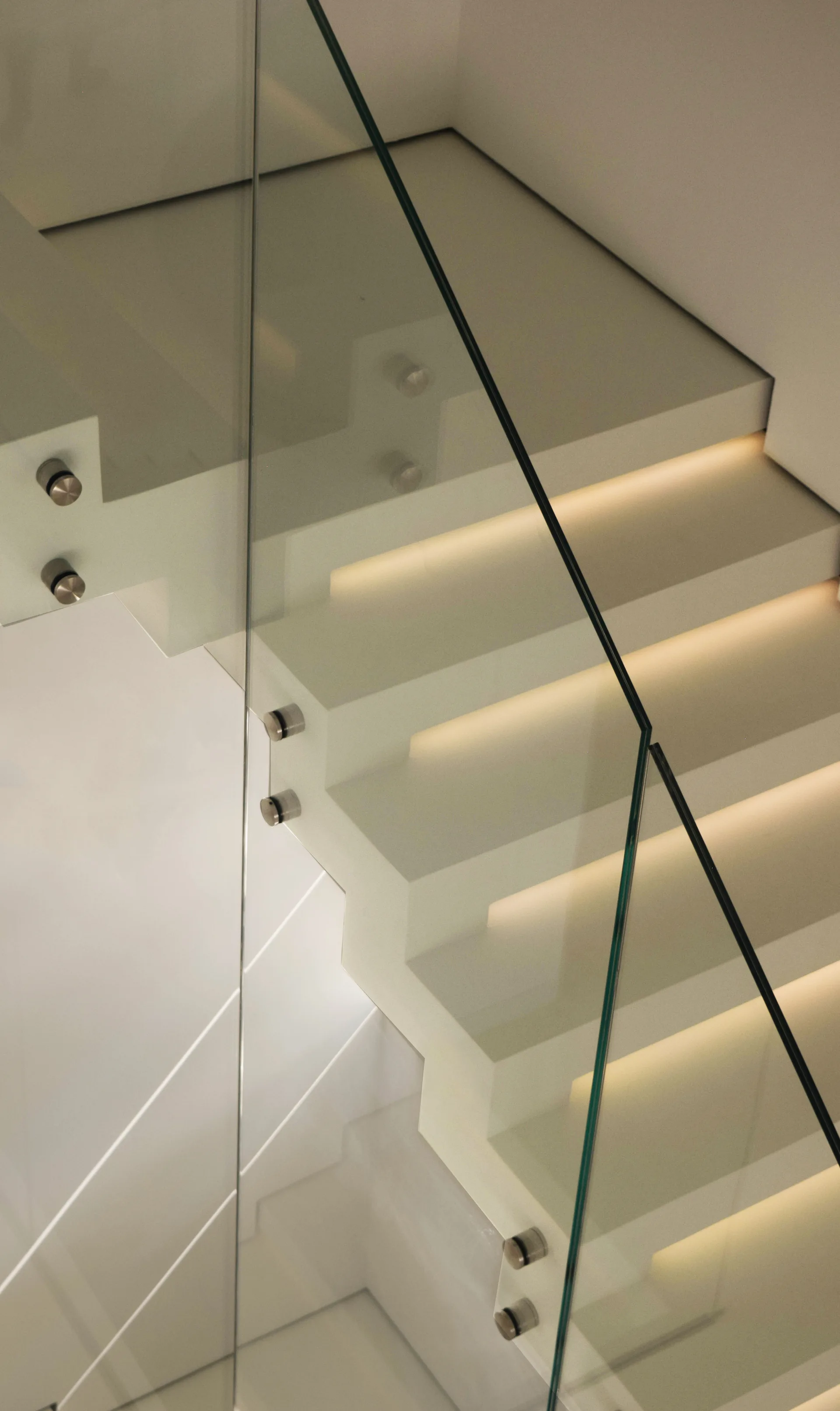 A minimalist floating staircase with smooth white treads, warm integrated lighting beneath each step, and clear glass railings.