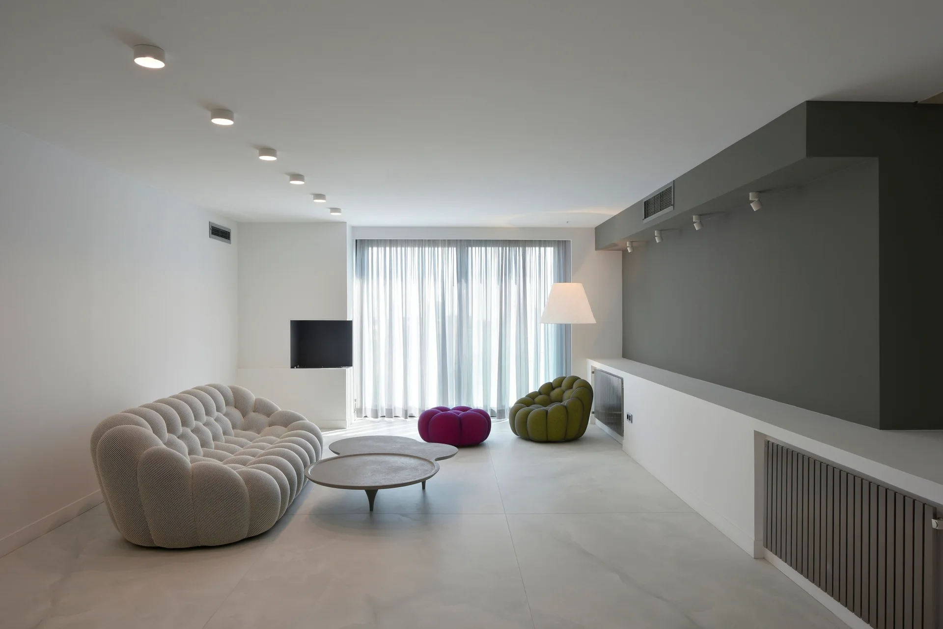 A minimalist living room featuring a light-colored tufted sofa, organic gray coffee table, and purple and olive green accent seating.