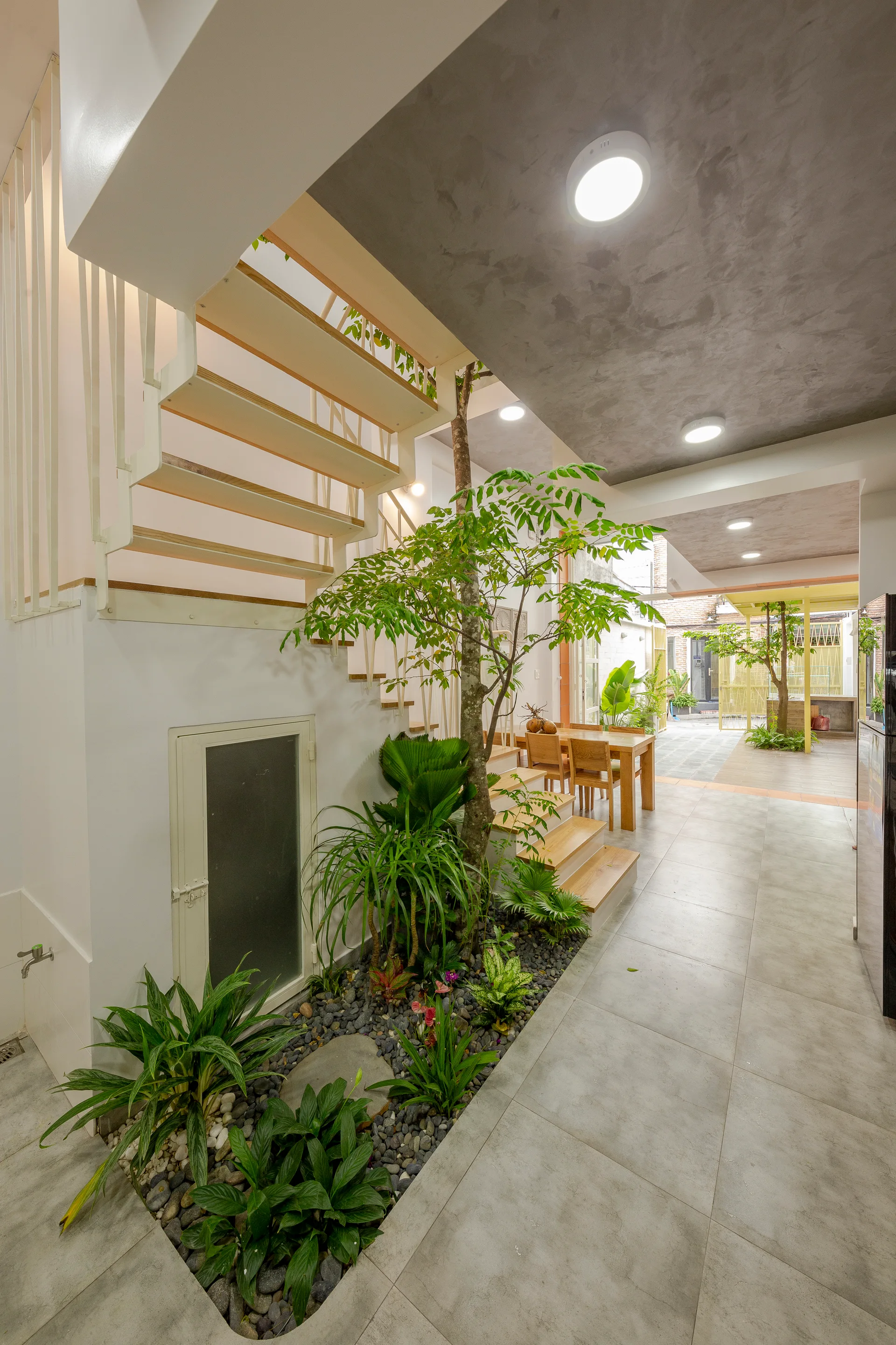 An indoor garden bed with pebbles and lush green plants sits at the base of an open-riser staircase with wooden treads.