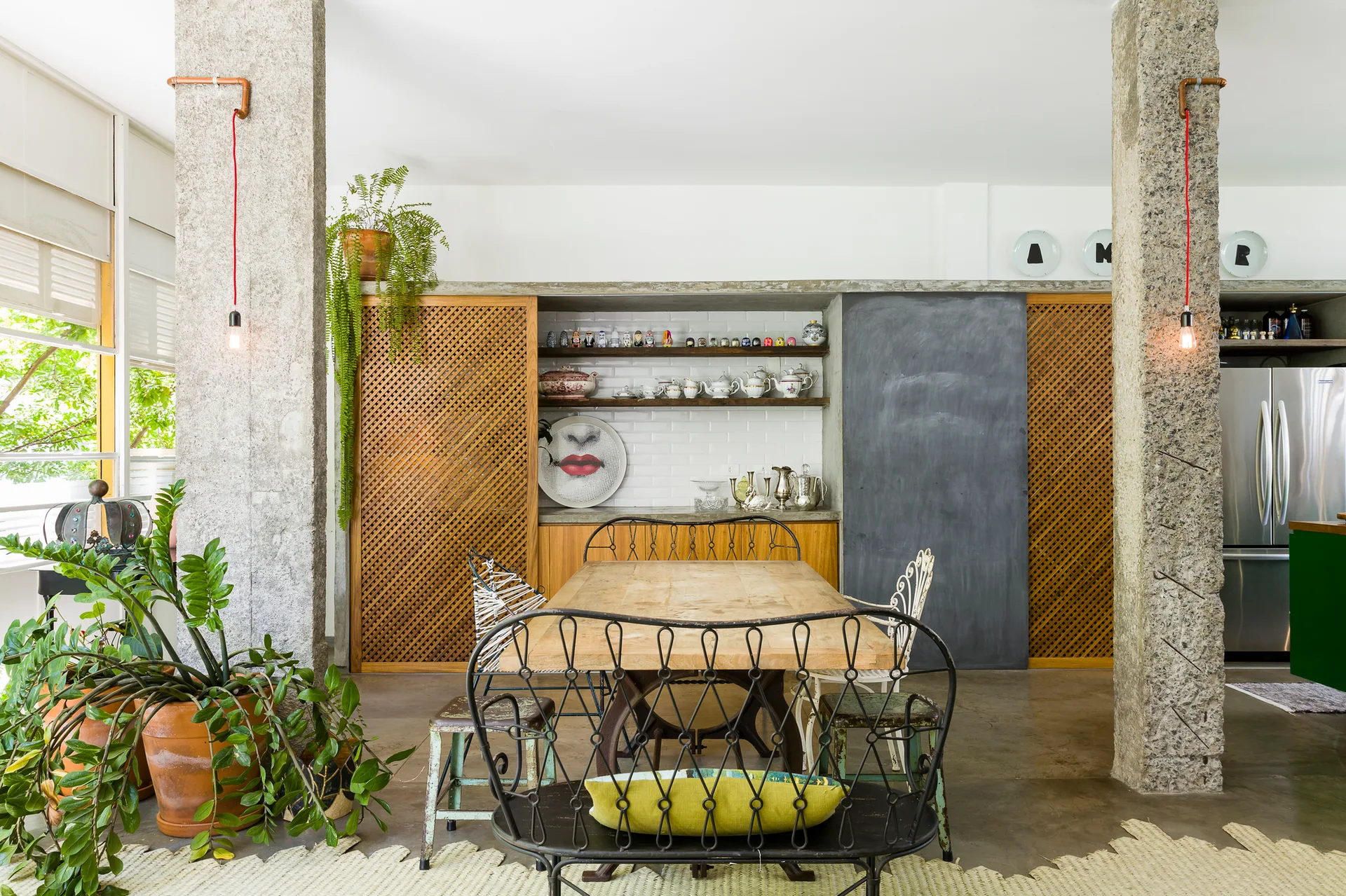 An eclectic dining room featuring a wooden table surrounded by metal chairs, flanked by two rough stone pillars and wooden lattice cabinets.