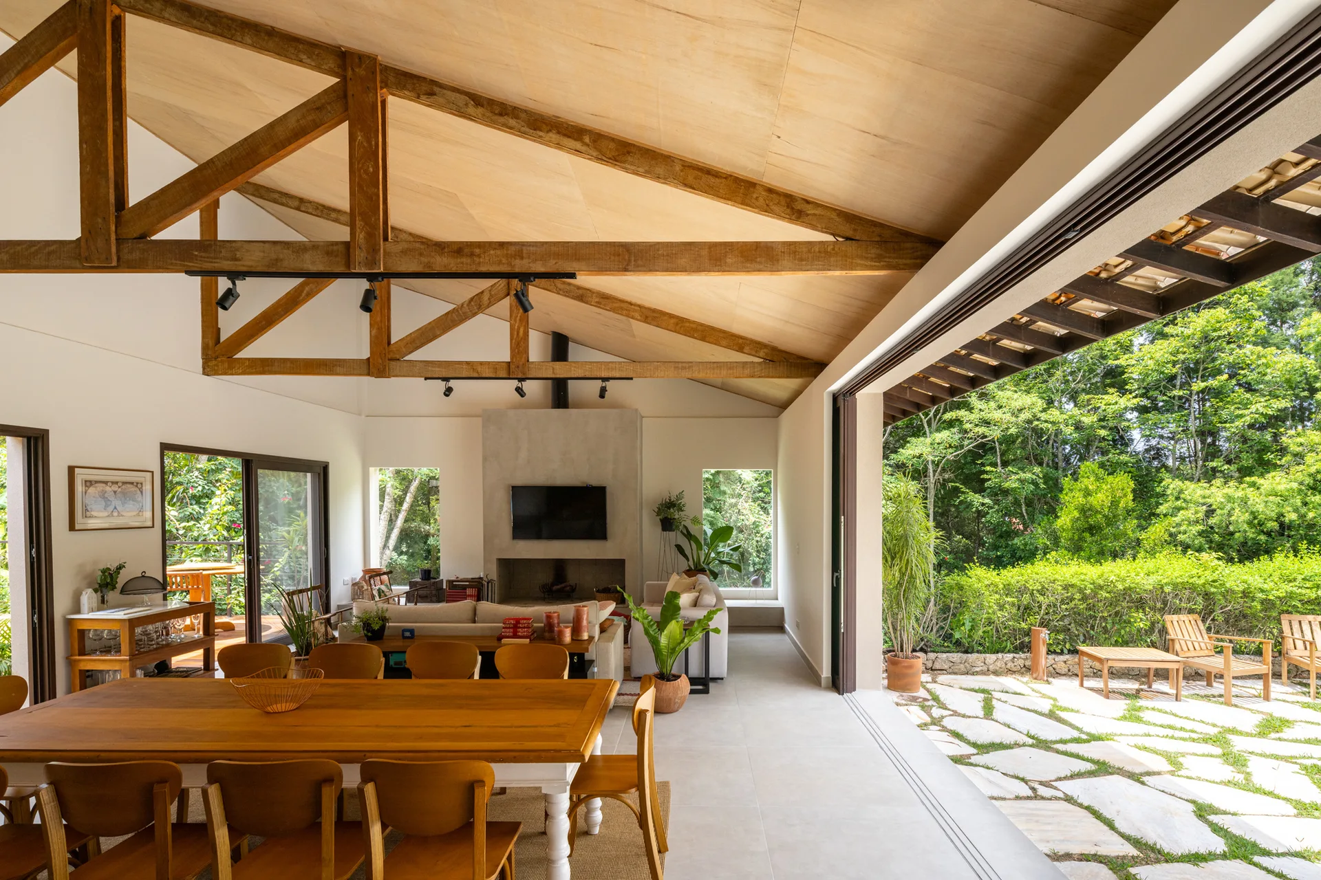 An open-concept living and dining area features exposed wood trusses on a vaulted ceiling, a concrete fireplace, and sliding doors opening to a stone patio.
