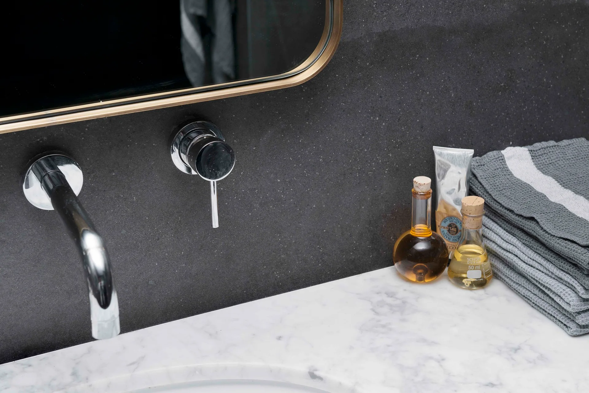 A close-up of a bathroom vanity featuring a white marble countertop, a wall-mounted chrome faucet, and a dark stone backsplash.