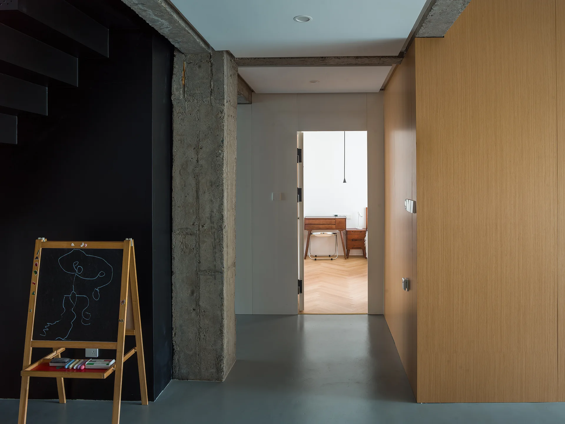 A modern hallway features a dark black wall, an exposed concrete pillar, and wood paneling leading to a bright bedroom with parquet floors.