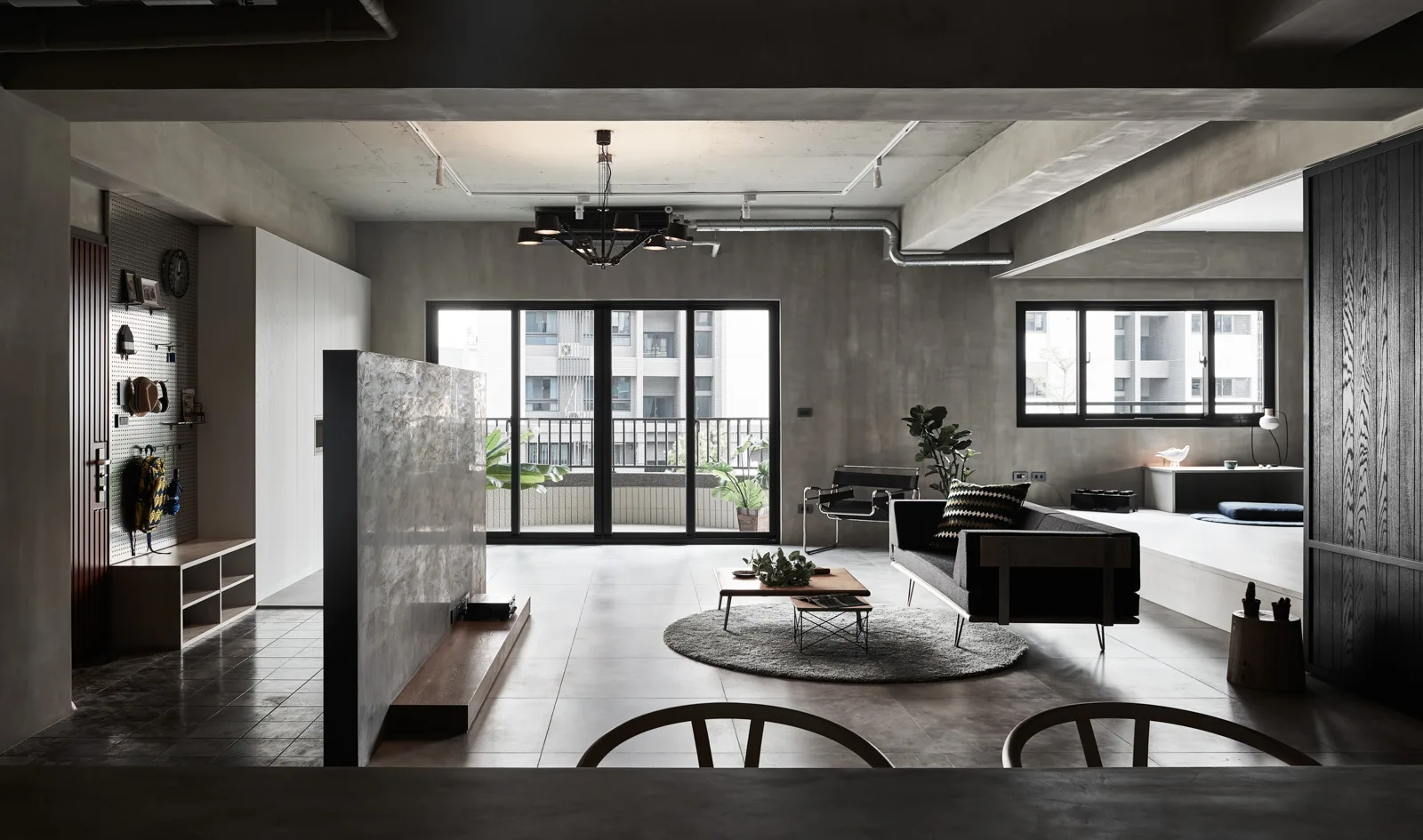 An industrial open plan living room with exposed concrete walls and ceiling, featuring a grey partition, black sofa, and large windows.