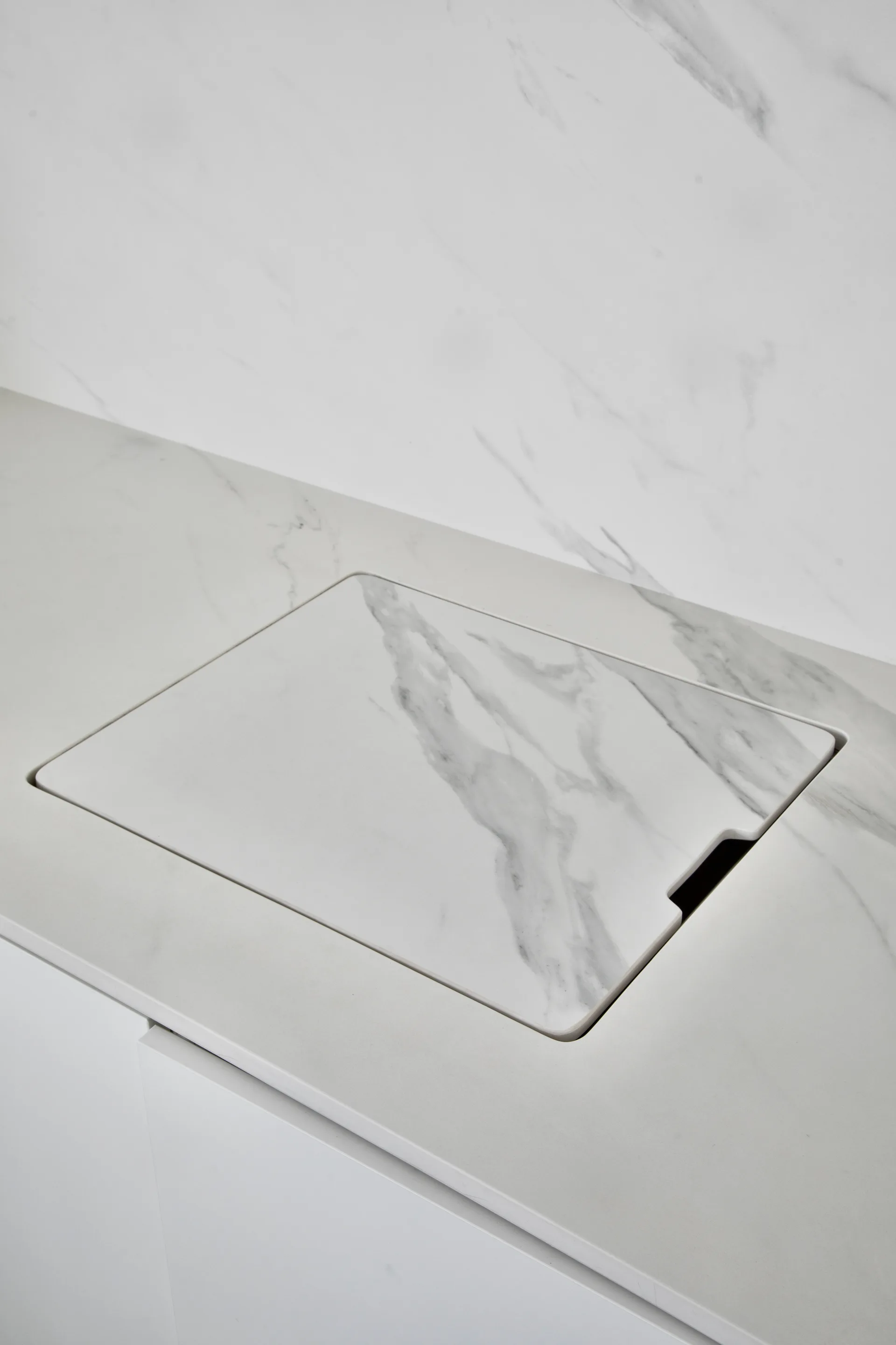A close-up of a white veined marble countertop with a matching flush-mounted square sink cover.