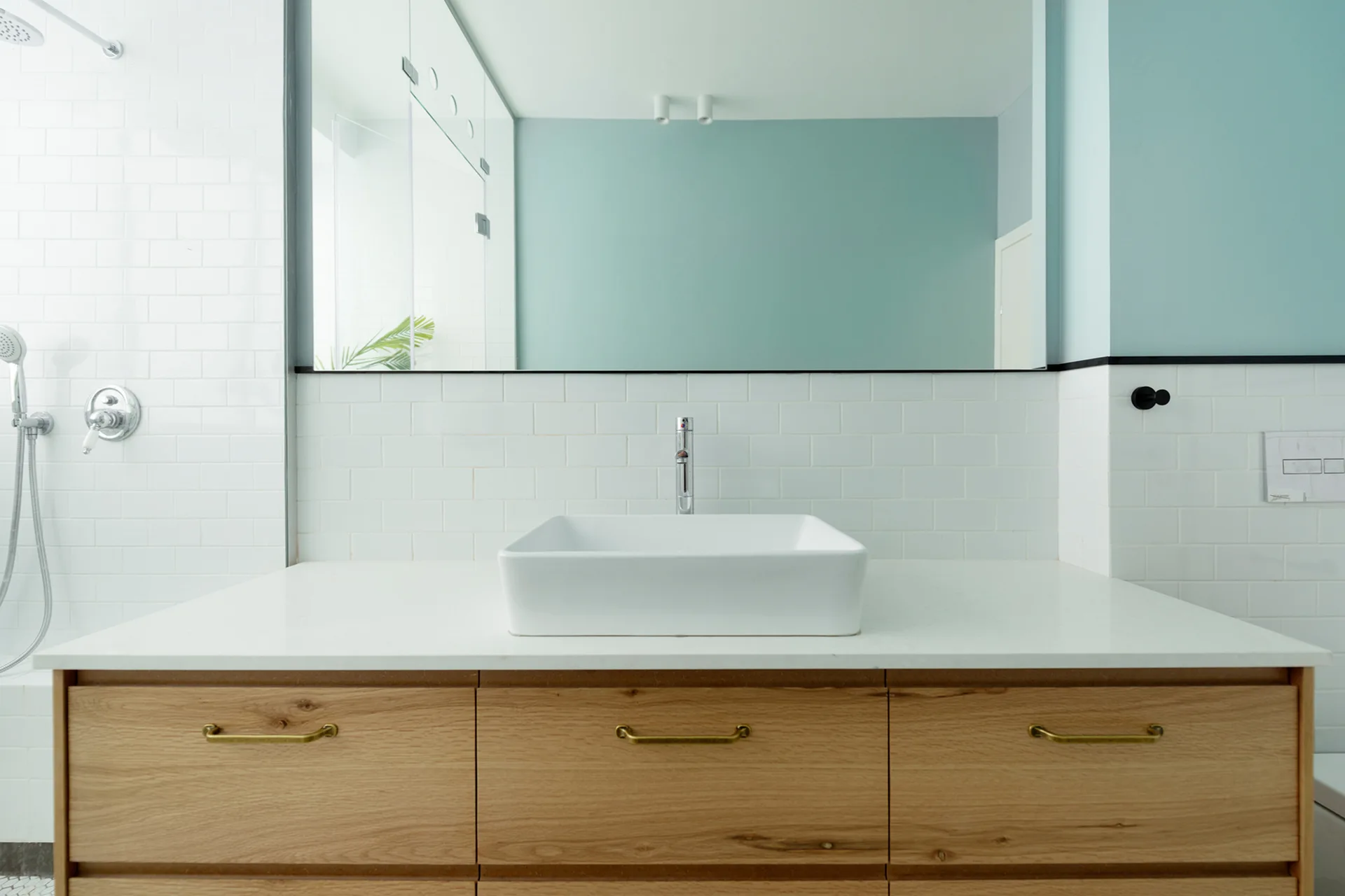 A wood bathroom vanity with a white vessel sink sits against a white subway tile backsplash below a large frameless mirror.