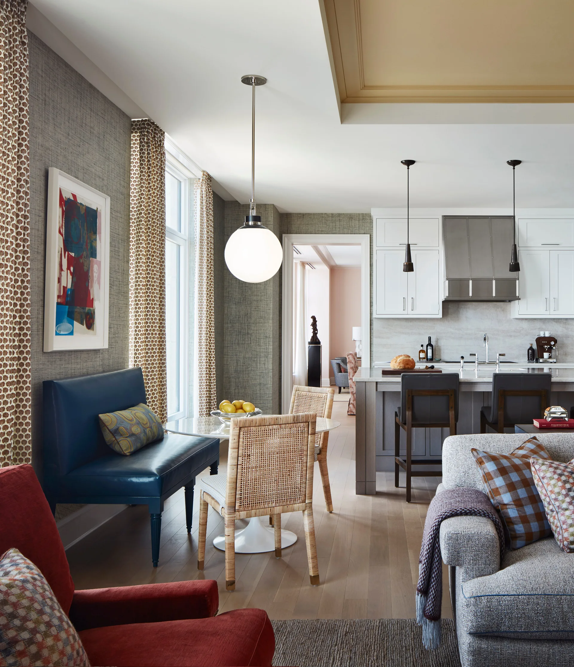 A transitional kitchen and dining area features a blue banquette, a round dining table with woven chairs, a kitchen island, and a globe pendant light.